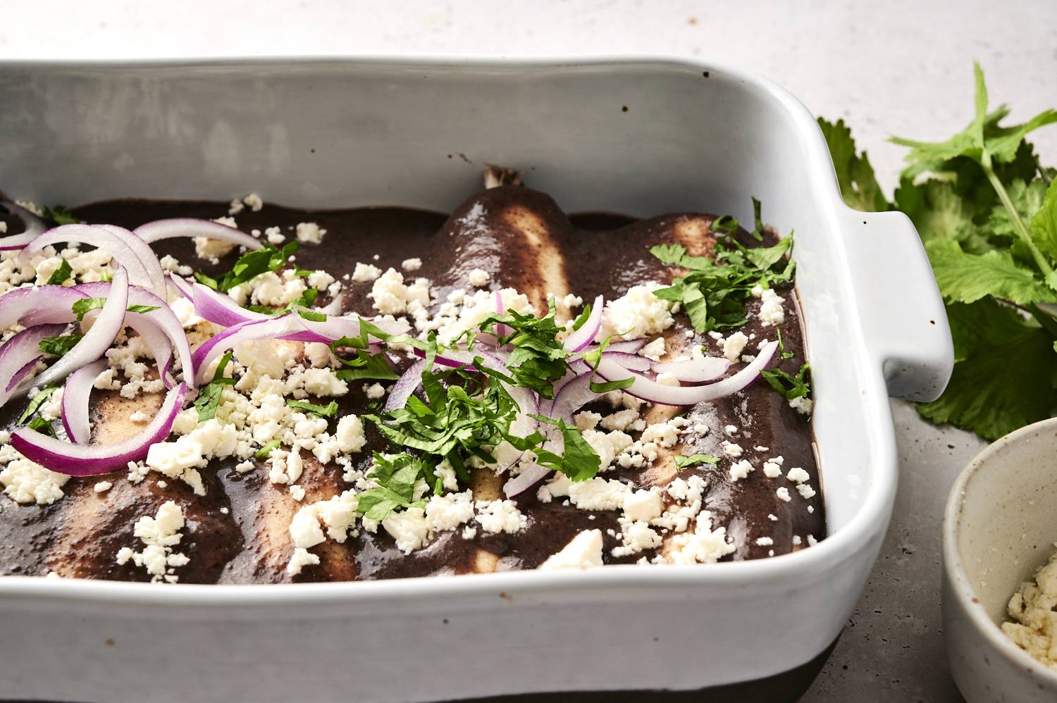 Enfrijoladas with creamy black bean sauce in a baking dish with cilantro, red onions, and queso fresco.