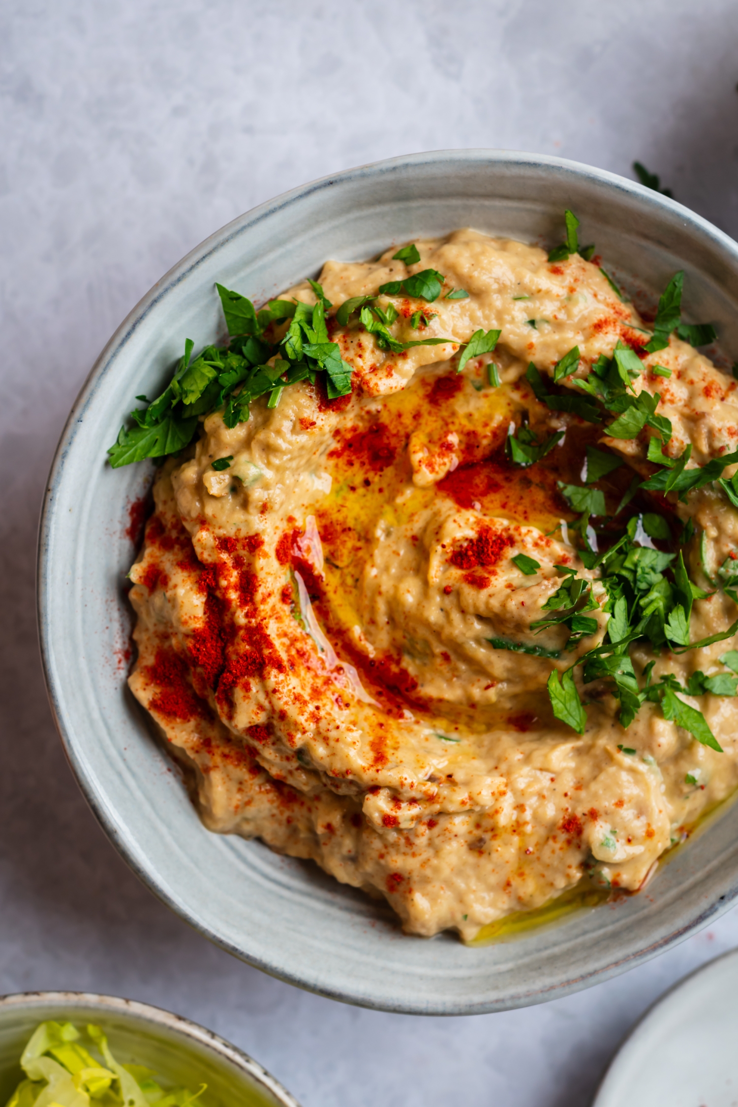 Eggplant baba ganoush in a bowl with fresh parsley, lemon, and paprika.