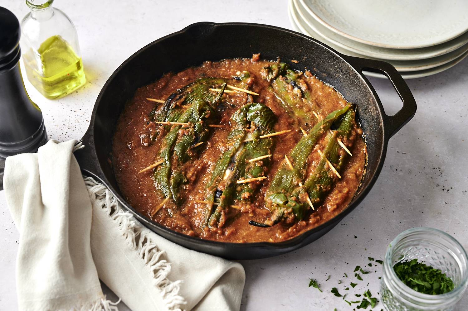 Chiles rellenos cooking in a cast iron skillet with toothpicks securing the peppers, surrounded by a savory sauce.
