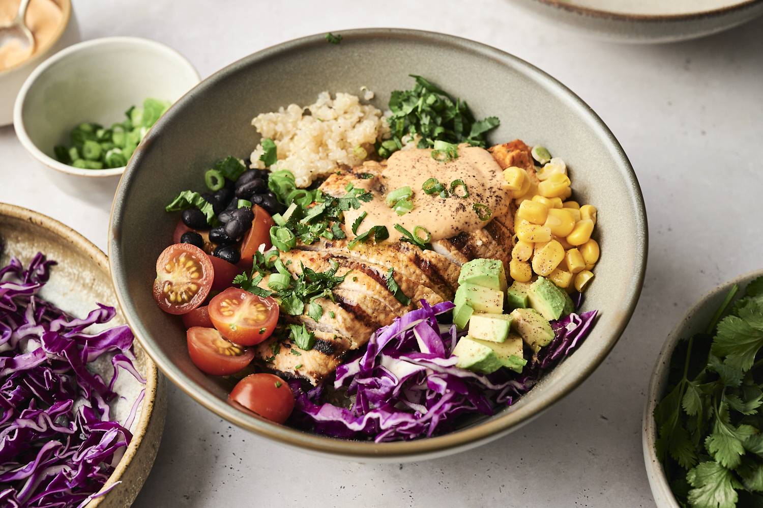 A Chipotle ranch chicken bowl with grilled chicken, quinoa, corn, avocado, tomatoes, black beans, red cabbage, and a creamy sauce.