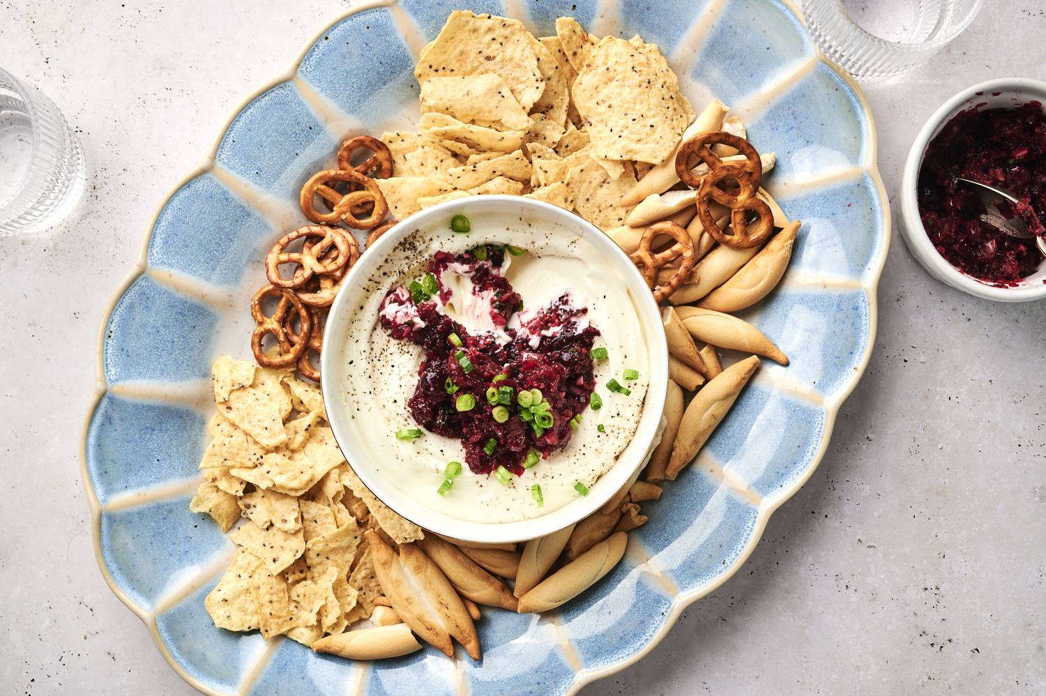 Cranberry jalapeno cream cheese dip in a bowl on a platter surrounded by chips.