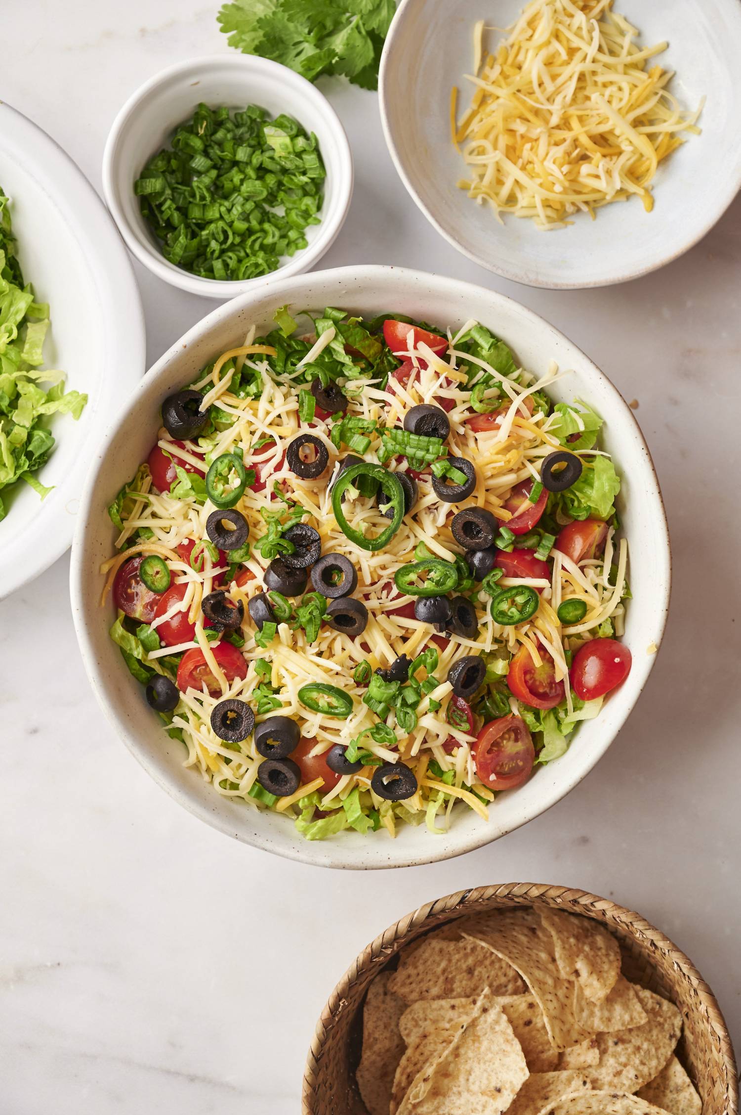 Lightened up taco dip in a bowl with salsa, beans, lettuce, cheese, jalapenos, and green onions.