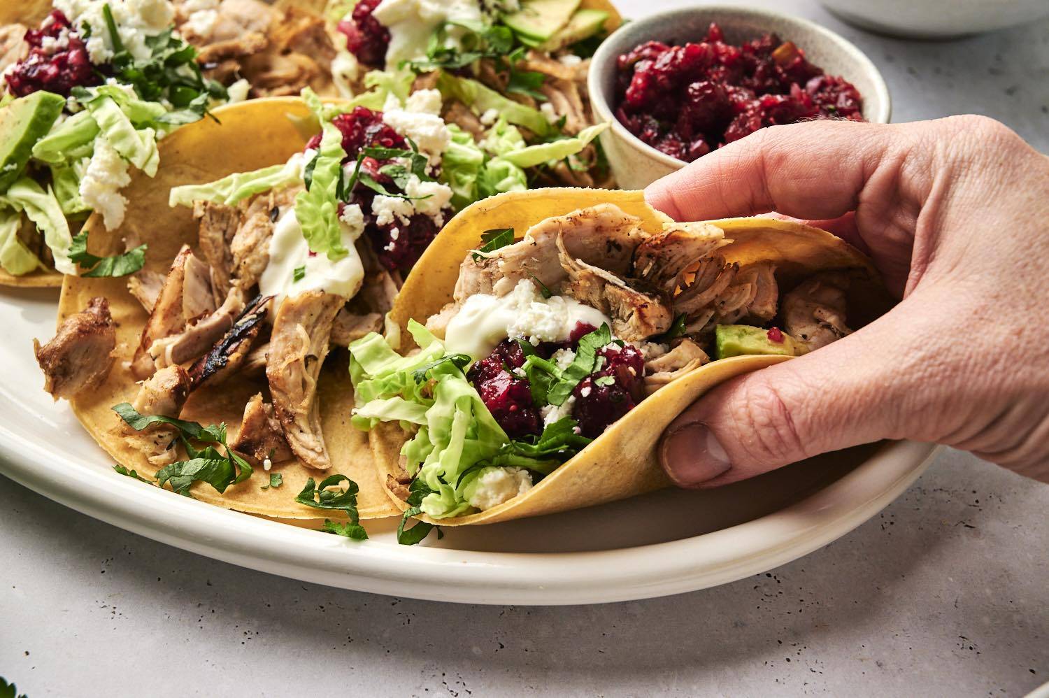 A hand grabbing a turkey taco off a plate.