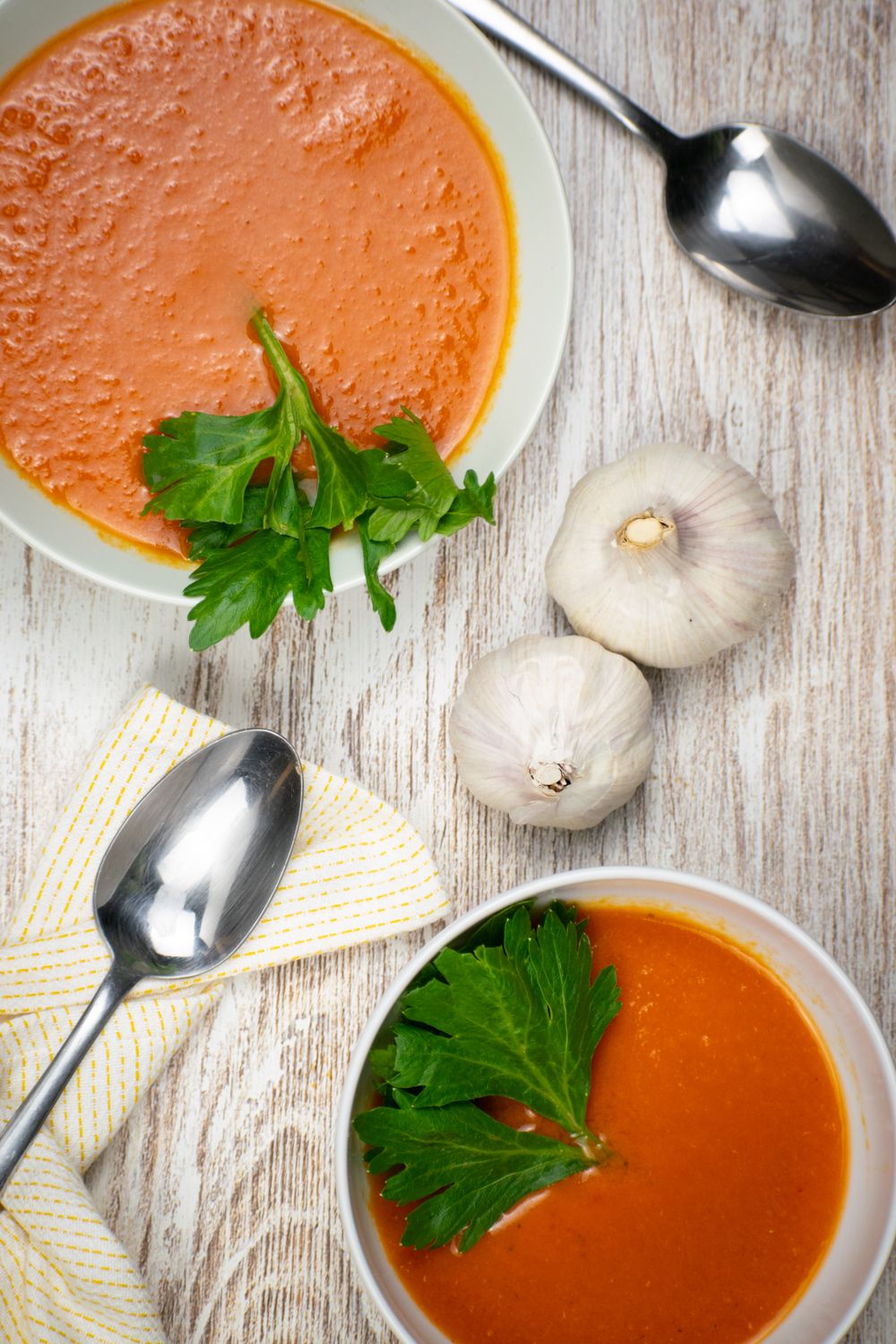 Chipotle tomsto soup in two bowls with cilantro and garlic bulbs on the side.