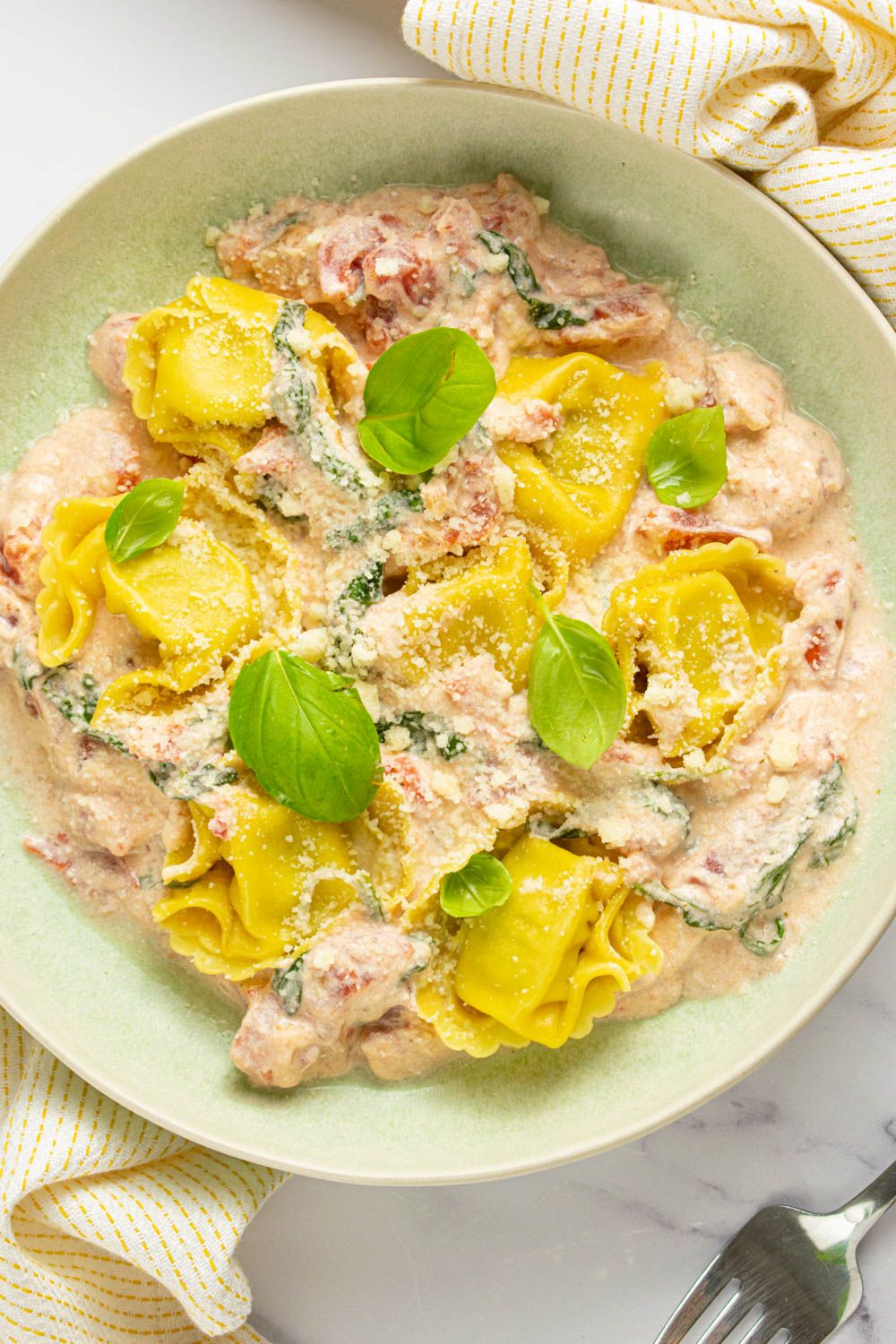 Cheese tortellini with tomatoes and basil in a bowl with Parmesan cheese.