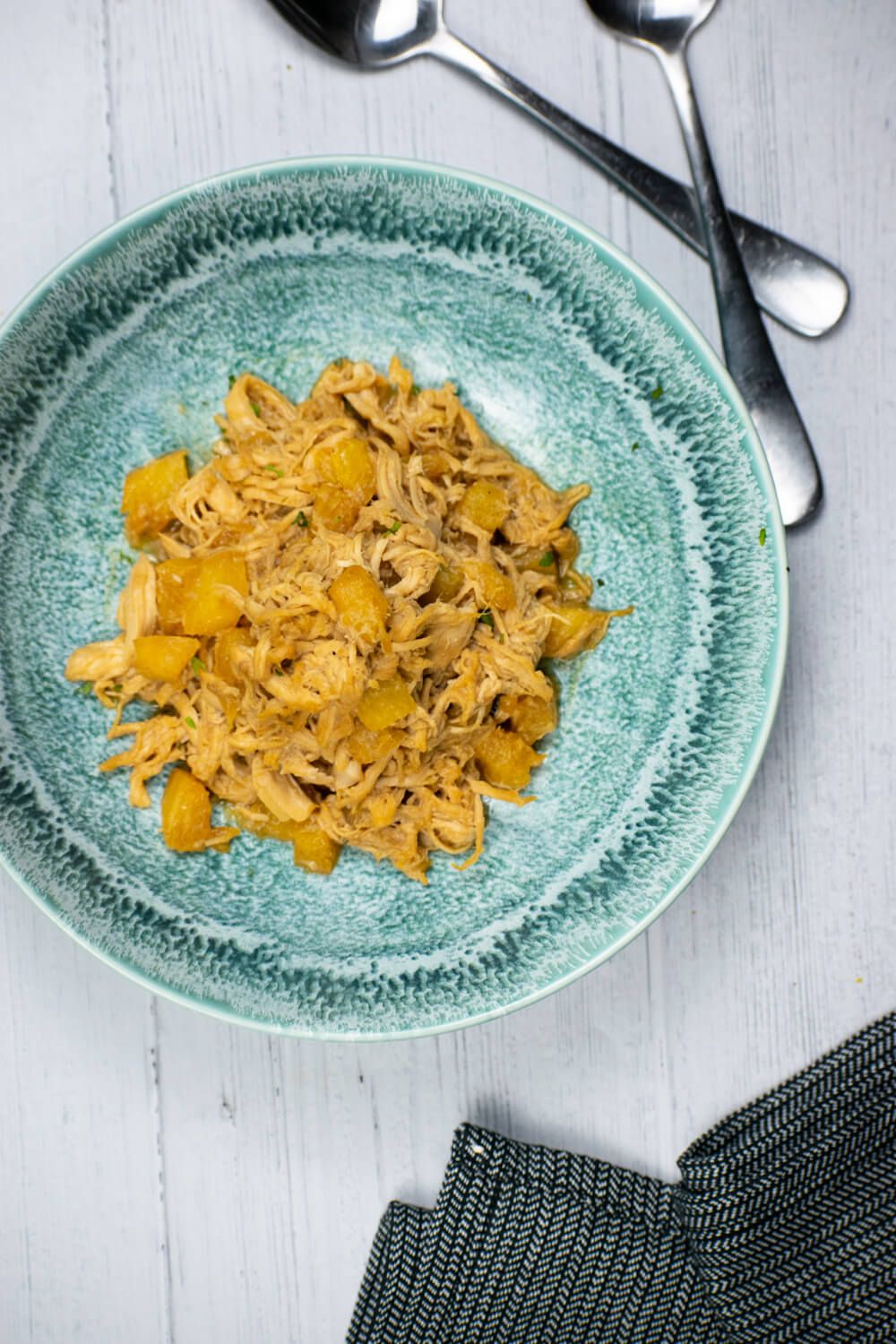 Crockpot Hawaiian chicken with pineapples in a blue bowl with two spoons on the side.
