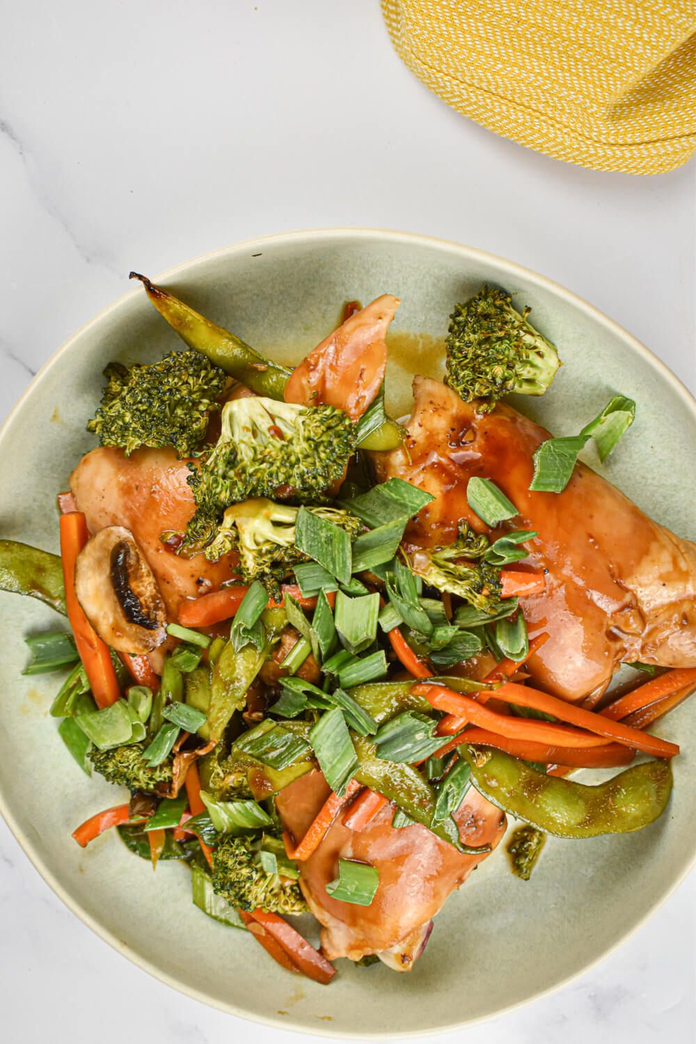 Teriyaki chicken thighs and vegetables in a bowl with sliced green onions.