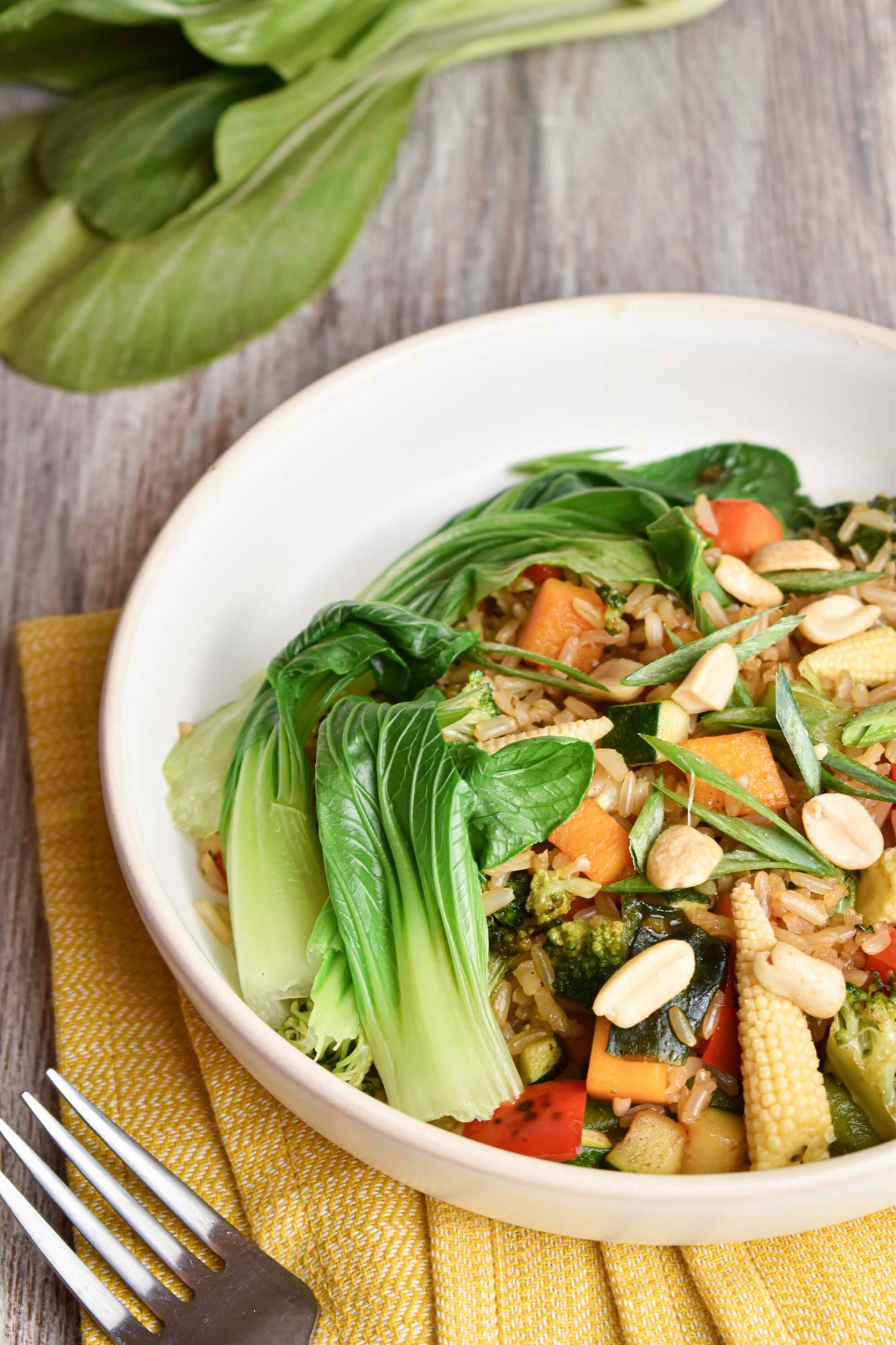 Vegetable and brown rice bowl with teriyaki sauce and peanuts on a white plate.