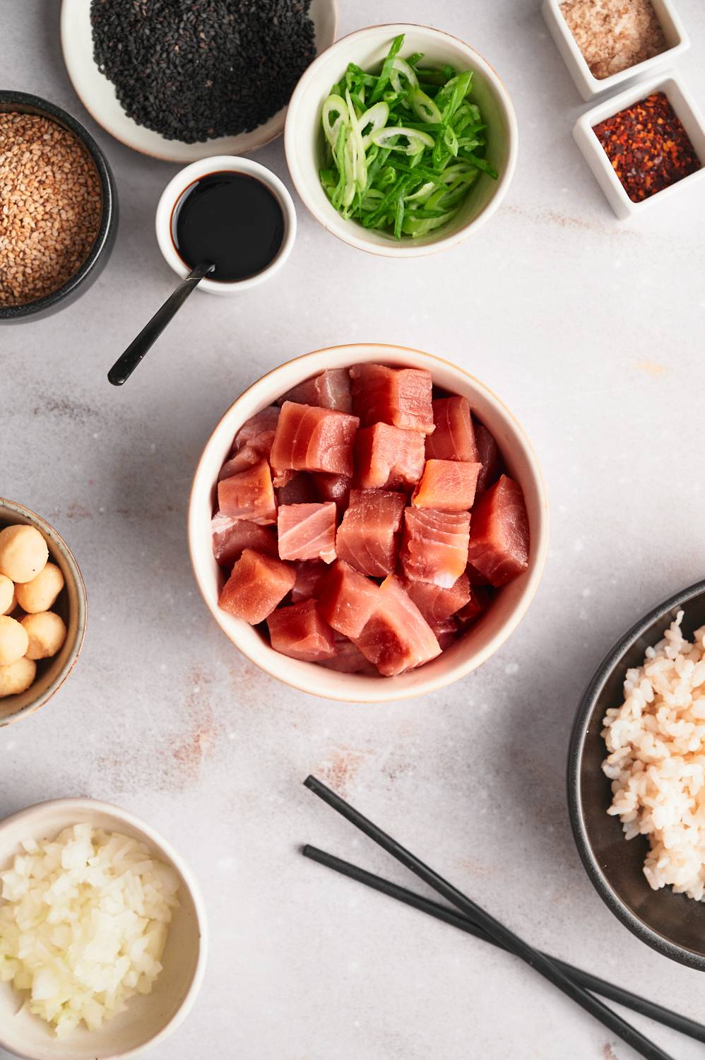 Ingredients for tuna poke including raw tuna, sesame seeds, green onions, soy sauce, sesame oil, and toppings.