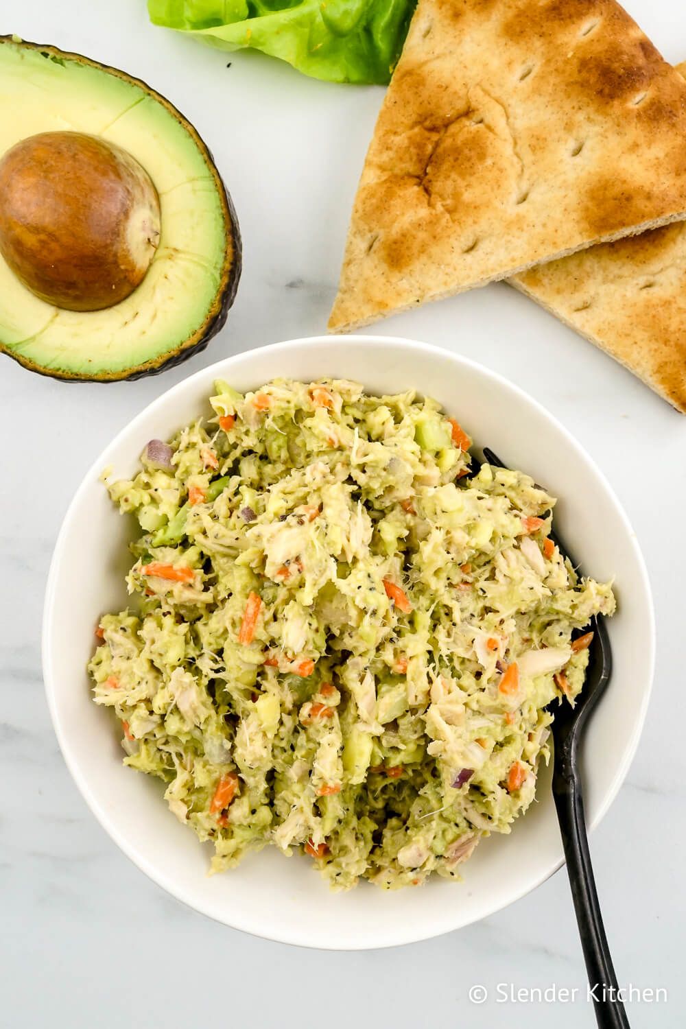 Tuna avocado salad in a bowl with an avocado and lettuce on the side.