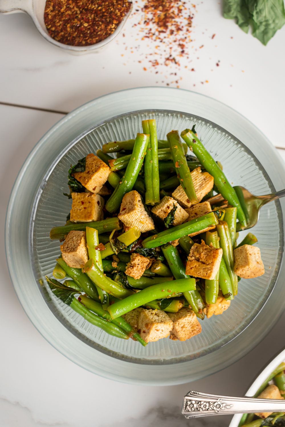 Stir fried tofu with basil and green beans in a bowl with red pepper flakes on the side.