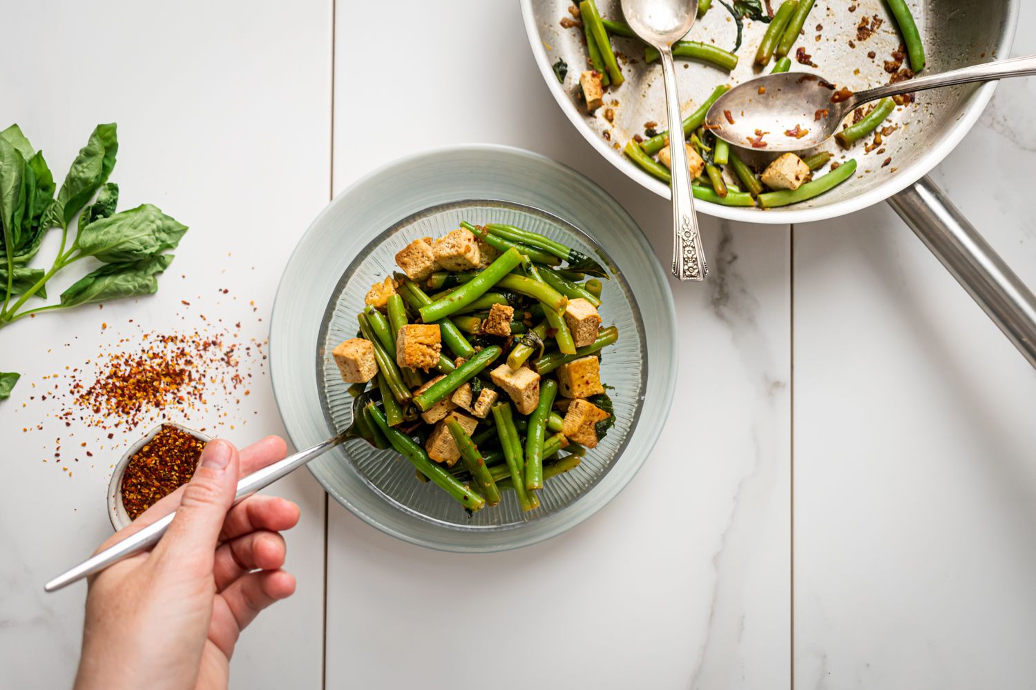 Tofu with a savory basil sauce served with green beans in a glass bowl with a fork.
