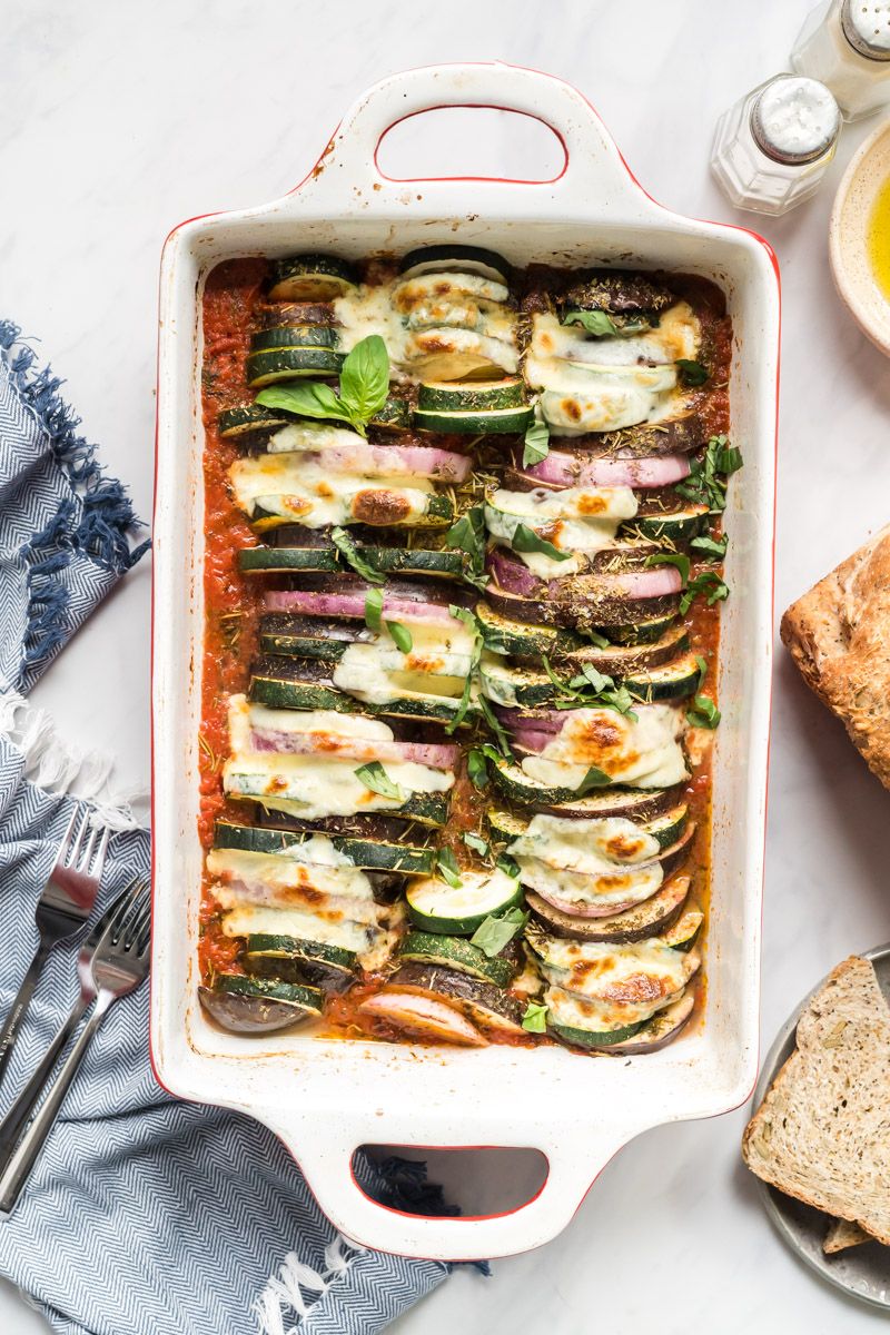 baked French Ratatouille in a dish with slices of eggplant, zucchini, summer squash, and red onion with tomatoes and fresh herbs.