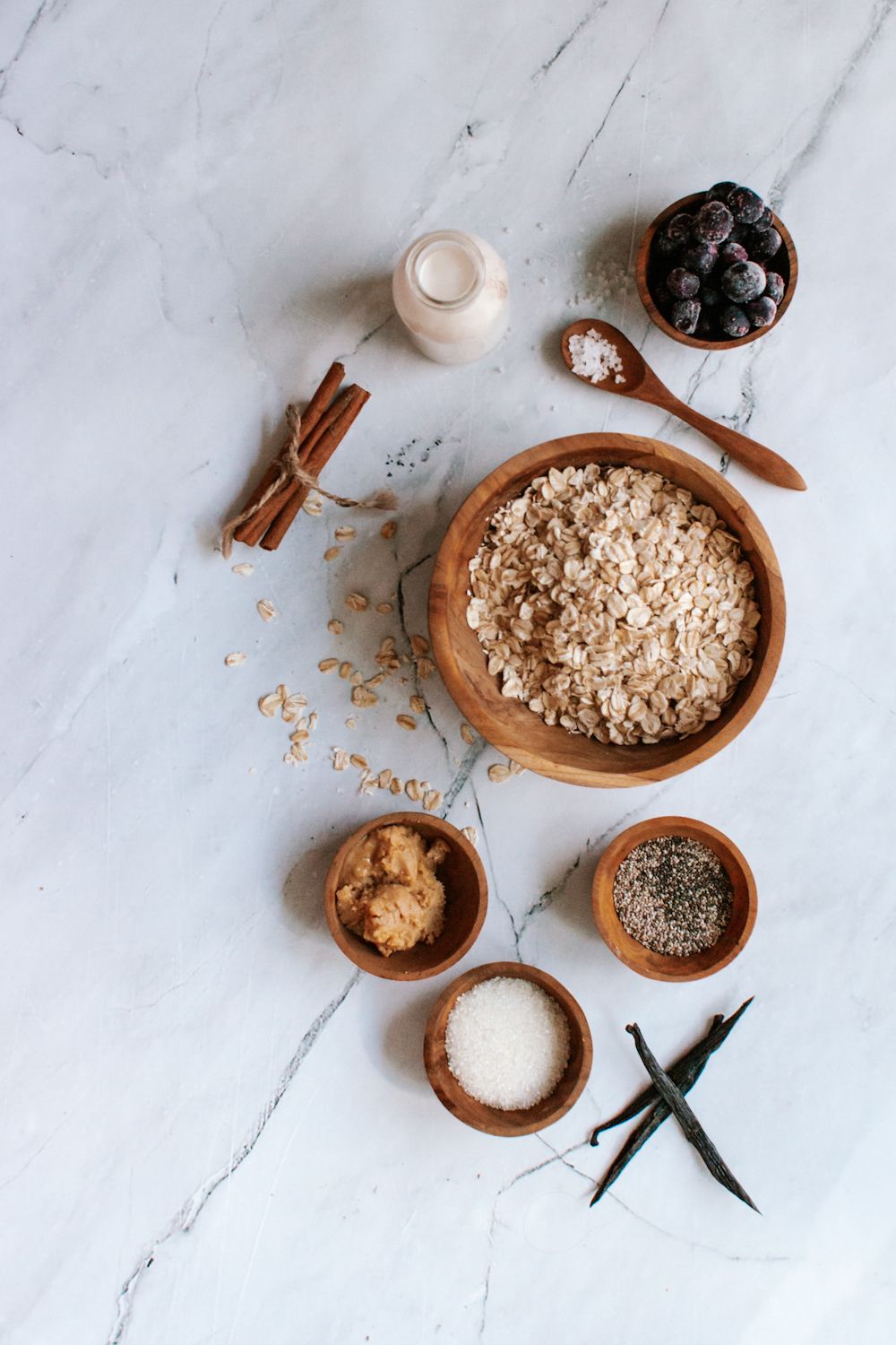 Ingredients for blueberry overnight oatmeal with almonds in a wooden dish with cinnamon, milk, and blueberries.