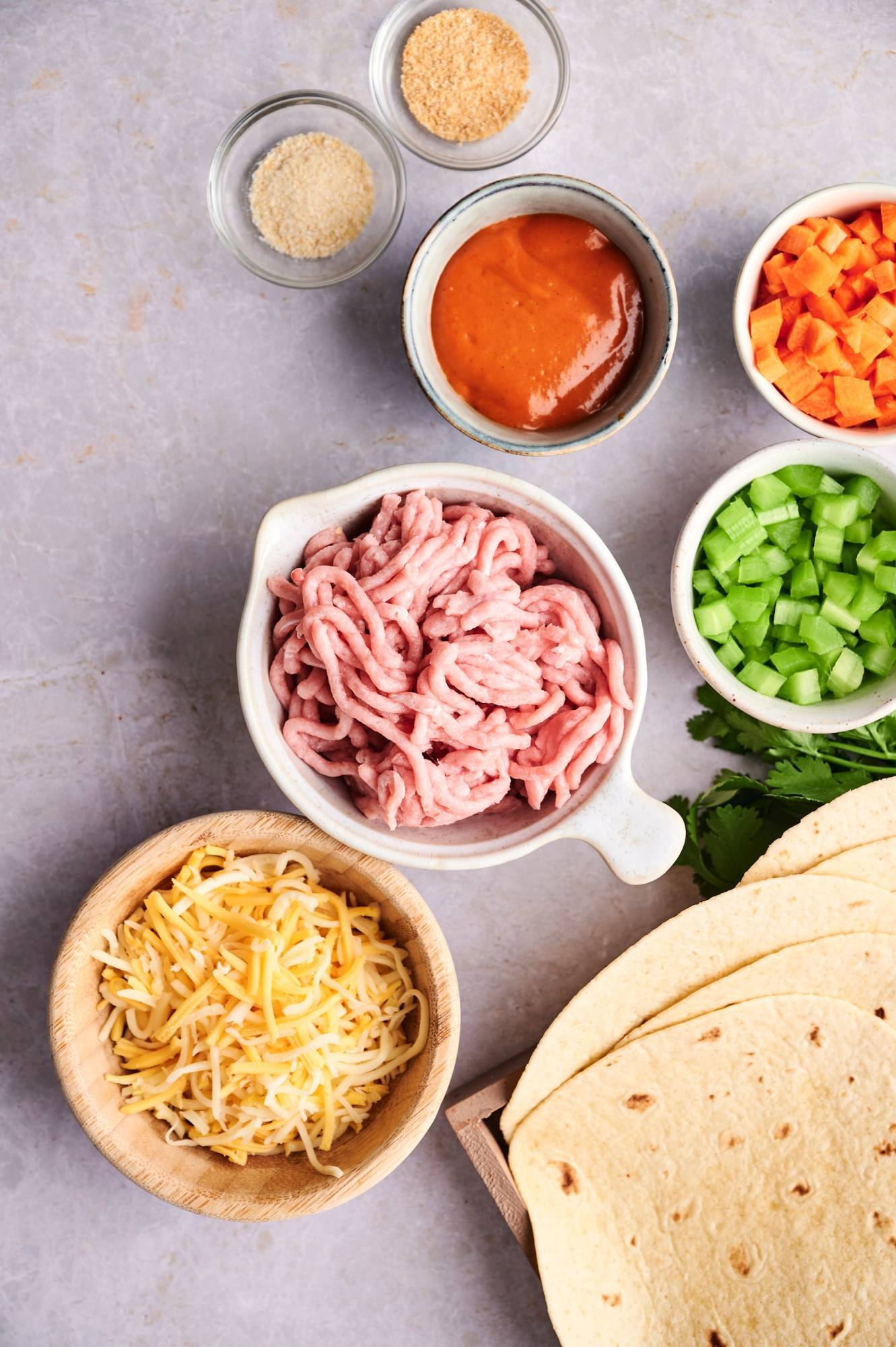 Ingredient for buffalo chicken quesadillas including ground chicken, carrots, celery, shredded cheese, buffalo sauce, and tortillas.