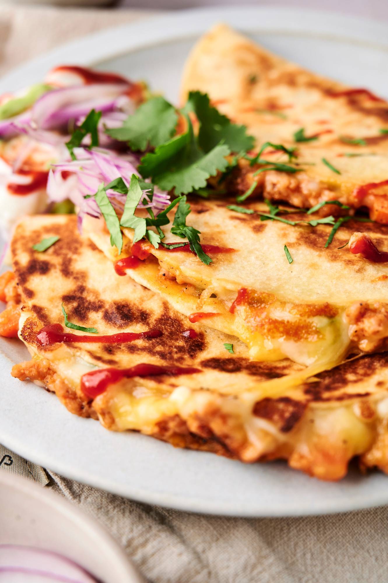 Crispy buffalo chicken quesadillas with melted cheese, buffalo sauce, and cilantro on a white plate.