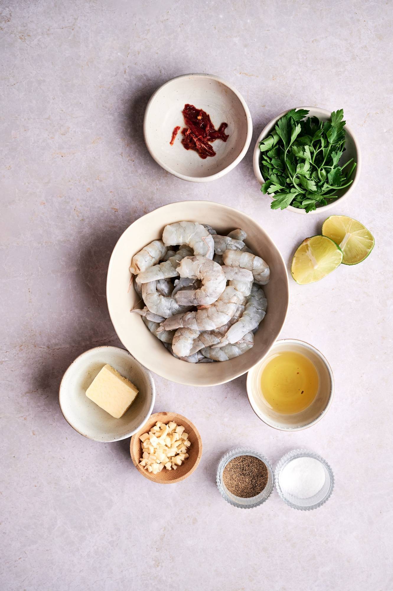 Ingredients for camaraones al ajillo including raw shrimp, olive oil, butter, garlic, chile peppers, parsley, and lime wedges.