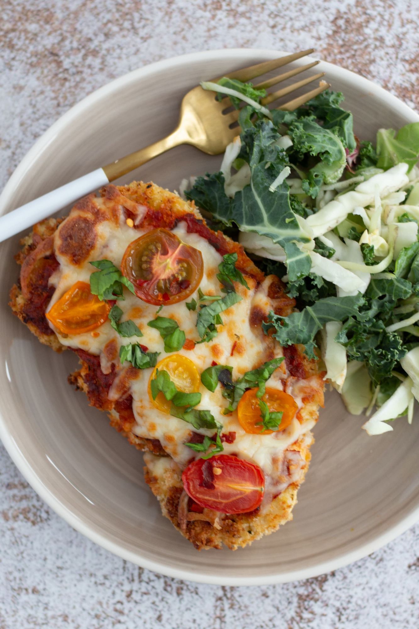 Vegetarian cauliflower parmesan topped with cherry tomatoes, basil, and melted cheese served with salad.