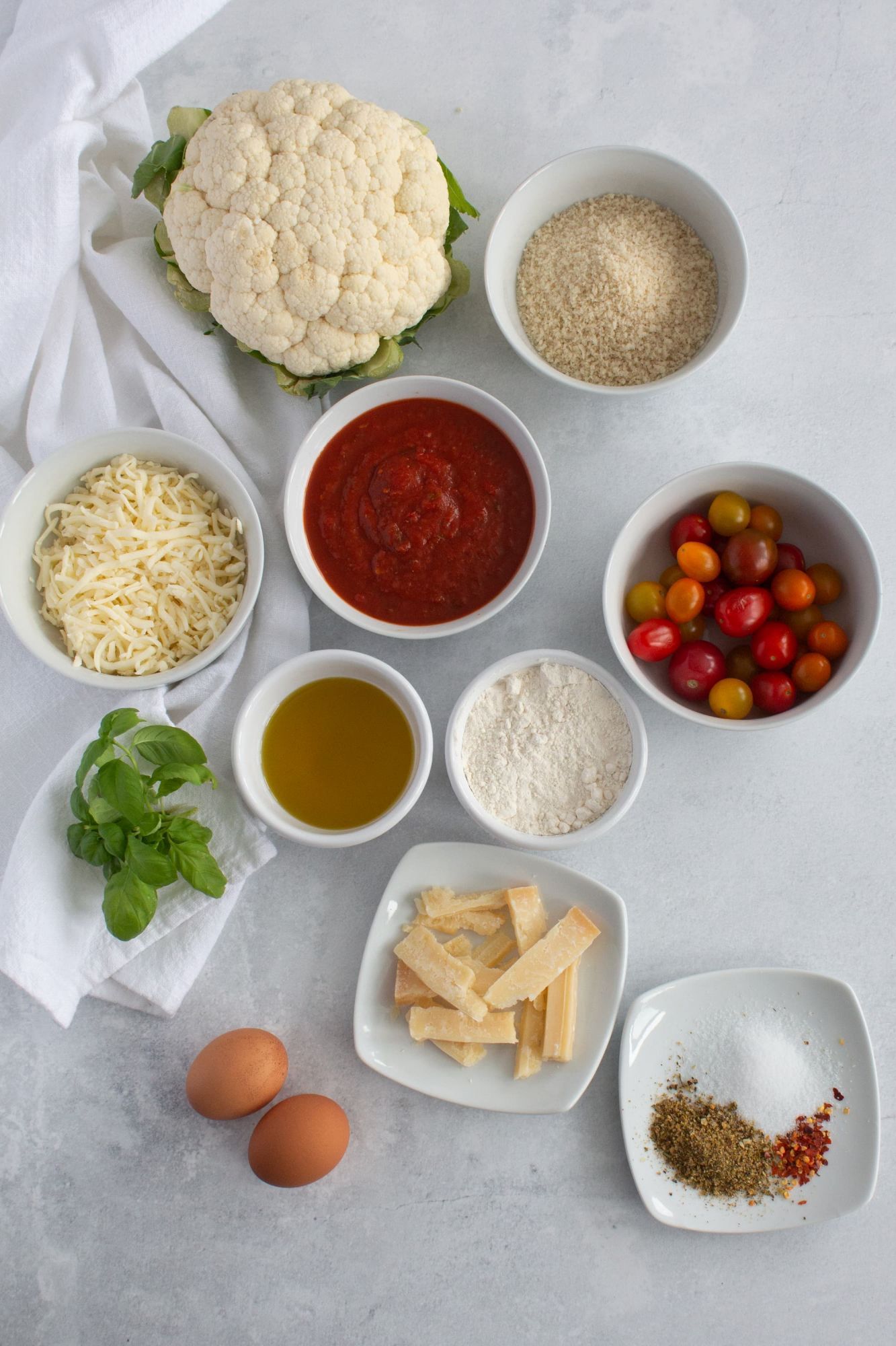 Ingredients for Cauliflower Parmesan including fresh cauliflower, marinara sauce, mozzarella cheese, spices, and basil.