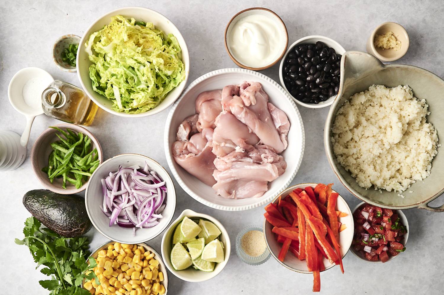 Ingredients for chicken and cauliflower rice bowls, including raw chicken, vegetables, black beans, corn, and seasonings.