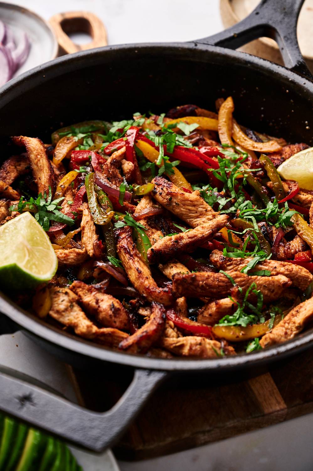 Skillet with chicken fajitas including seasoned chicken strips, bell peppers, red onions, and cilantro.
