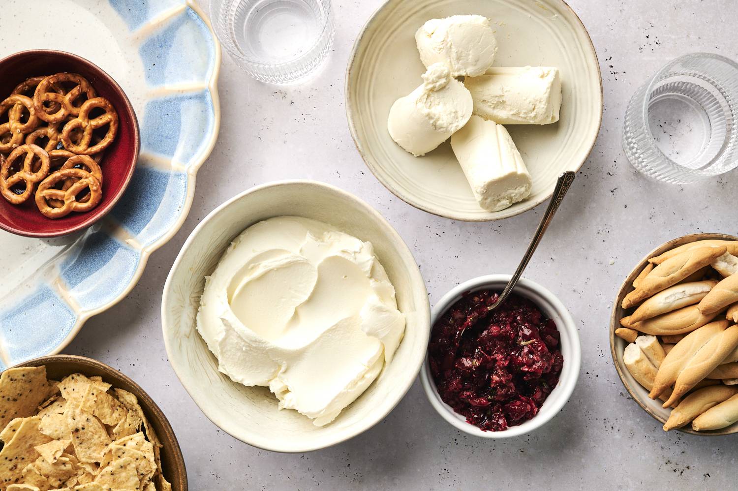 Ingredients needed to make cranberry cream cheese dip, including cranberries, jalapenos, goat cheese, cream cheese, cilantro, pretzels and more.