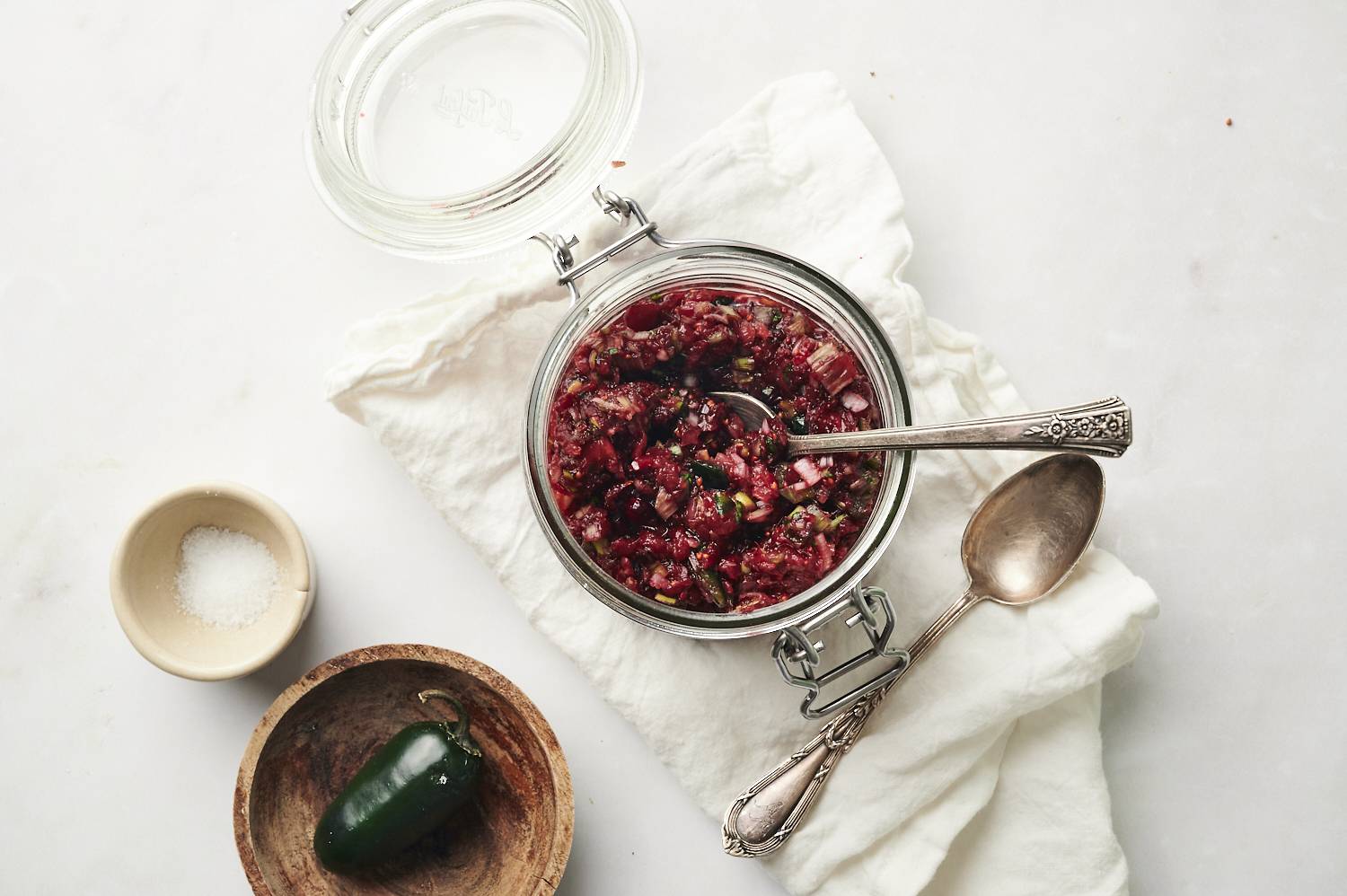 A bowl of cranberry relish, with jalapenos and a spoon off to the side.