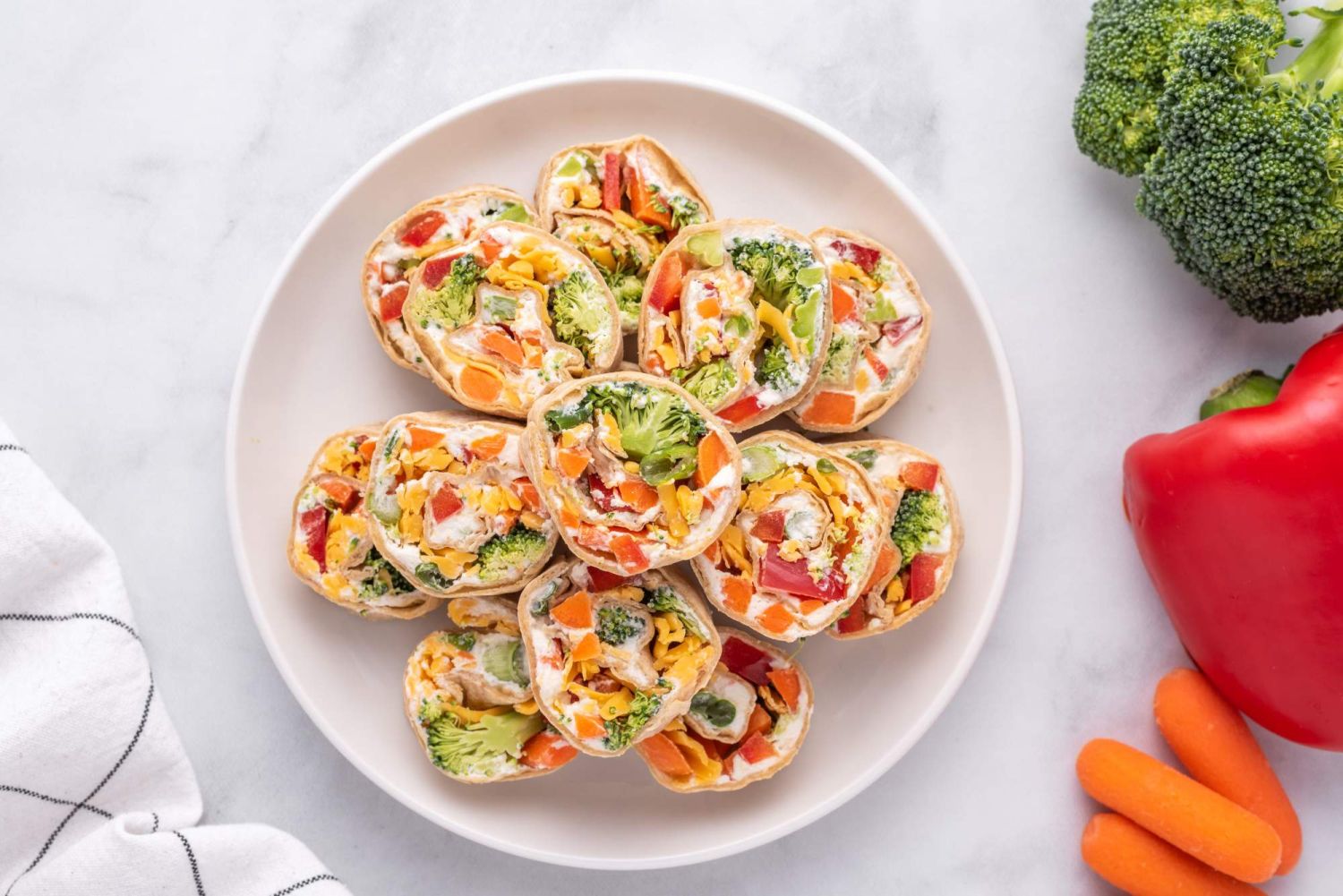 Ranch cream cheese and vegetable pinwheels in whole wheat tortillas cut into small pieces on a  plate.