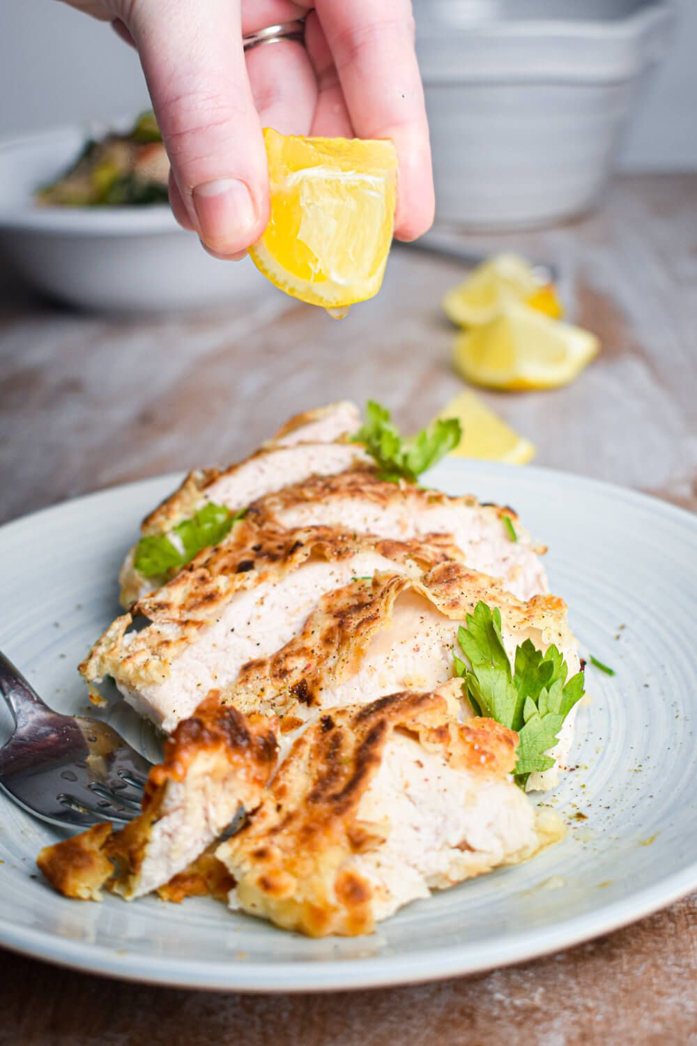 Oven Fried Buttermilk Chicken sliced on a plate with a hand squeezing lemon on top.