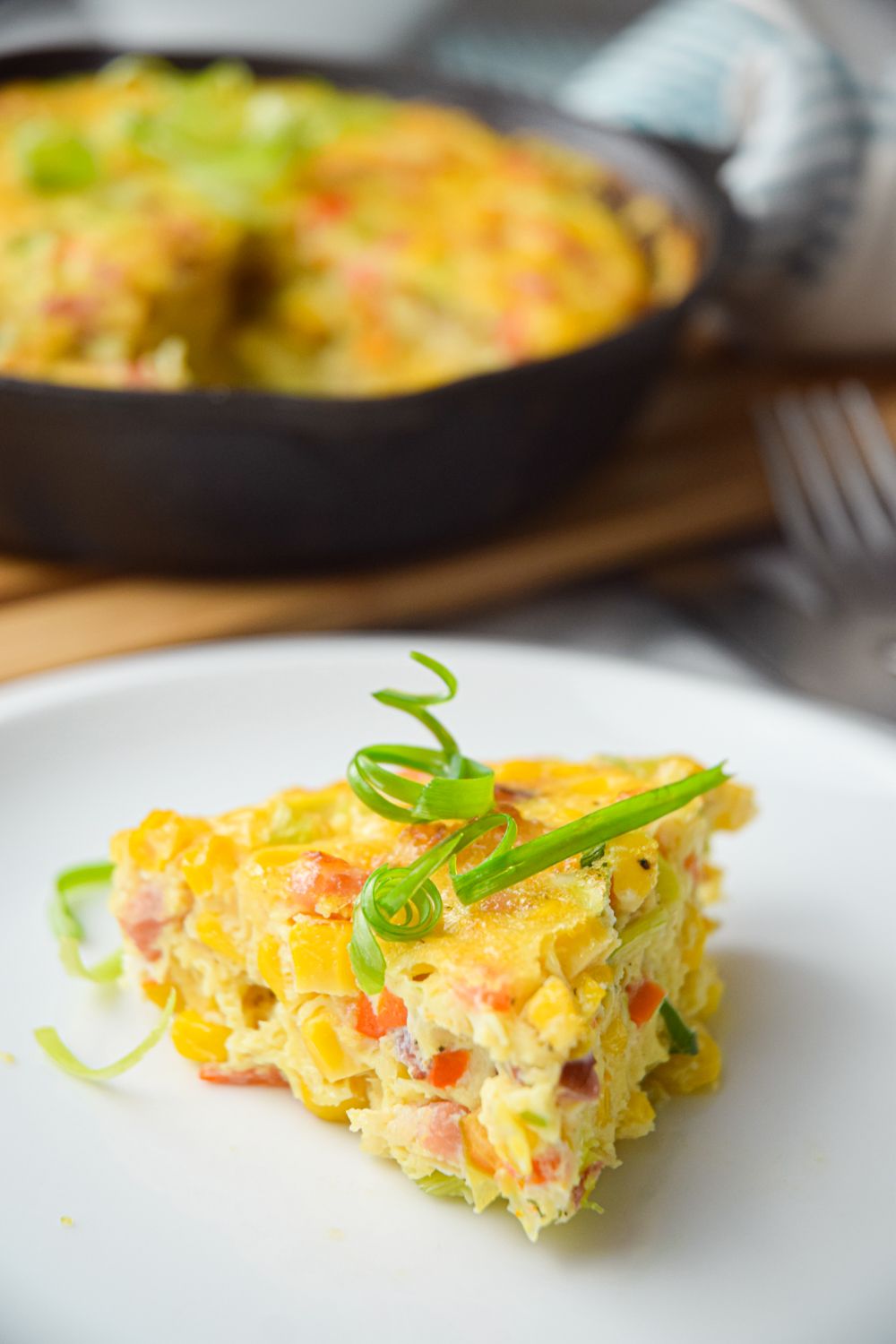 Bacon and corn pie with green onions in a skillet with one slice taken out on a plate.