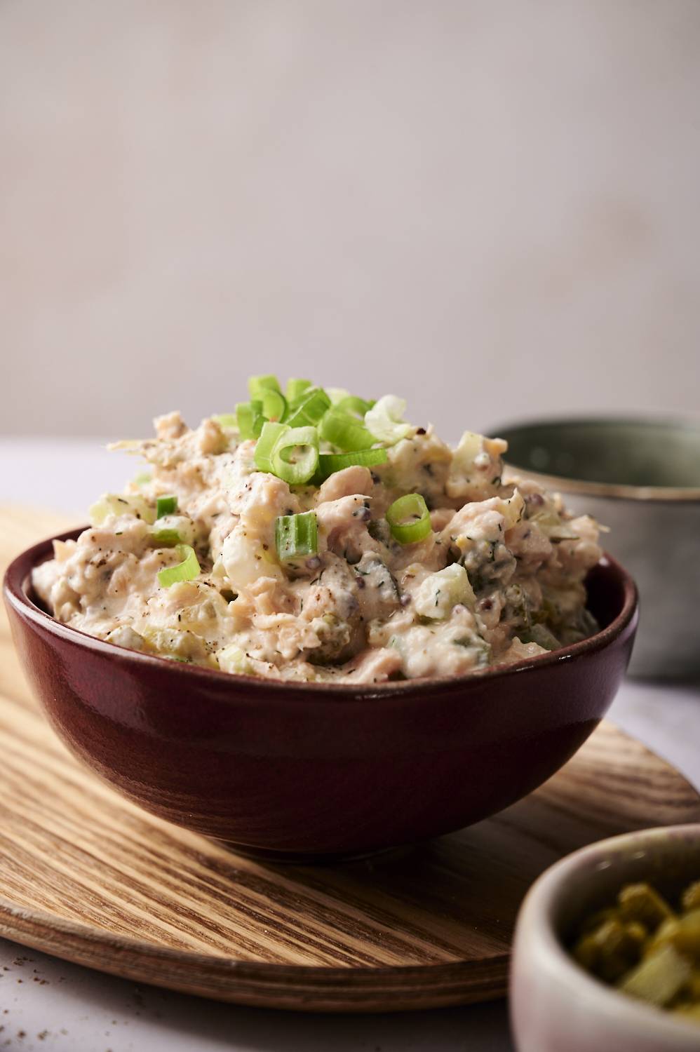 A vertical shot of a bowl of dill pickle salmon salad on a wooden board.