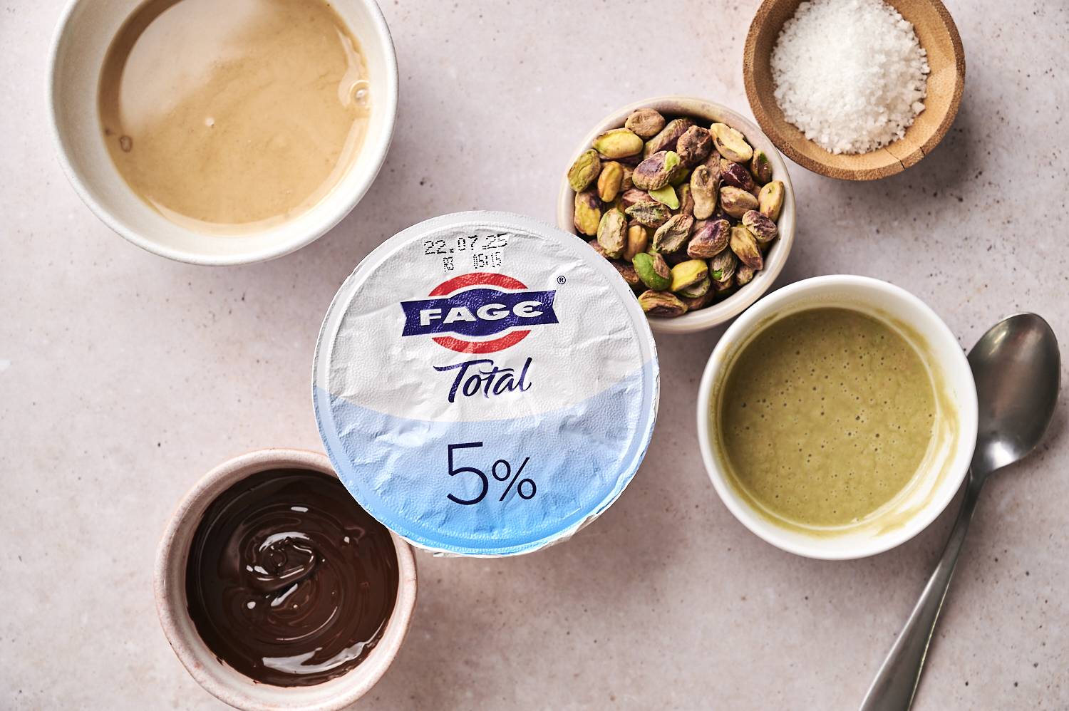 A top-down shot of the ingredients for Dubai chocolate yogurt cups, including a bowl of dates and a variety of nuts.