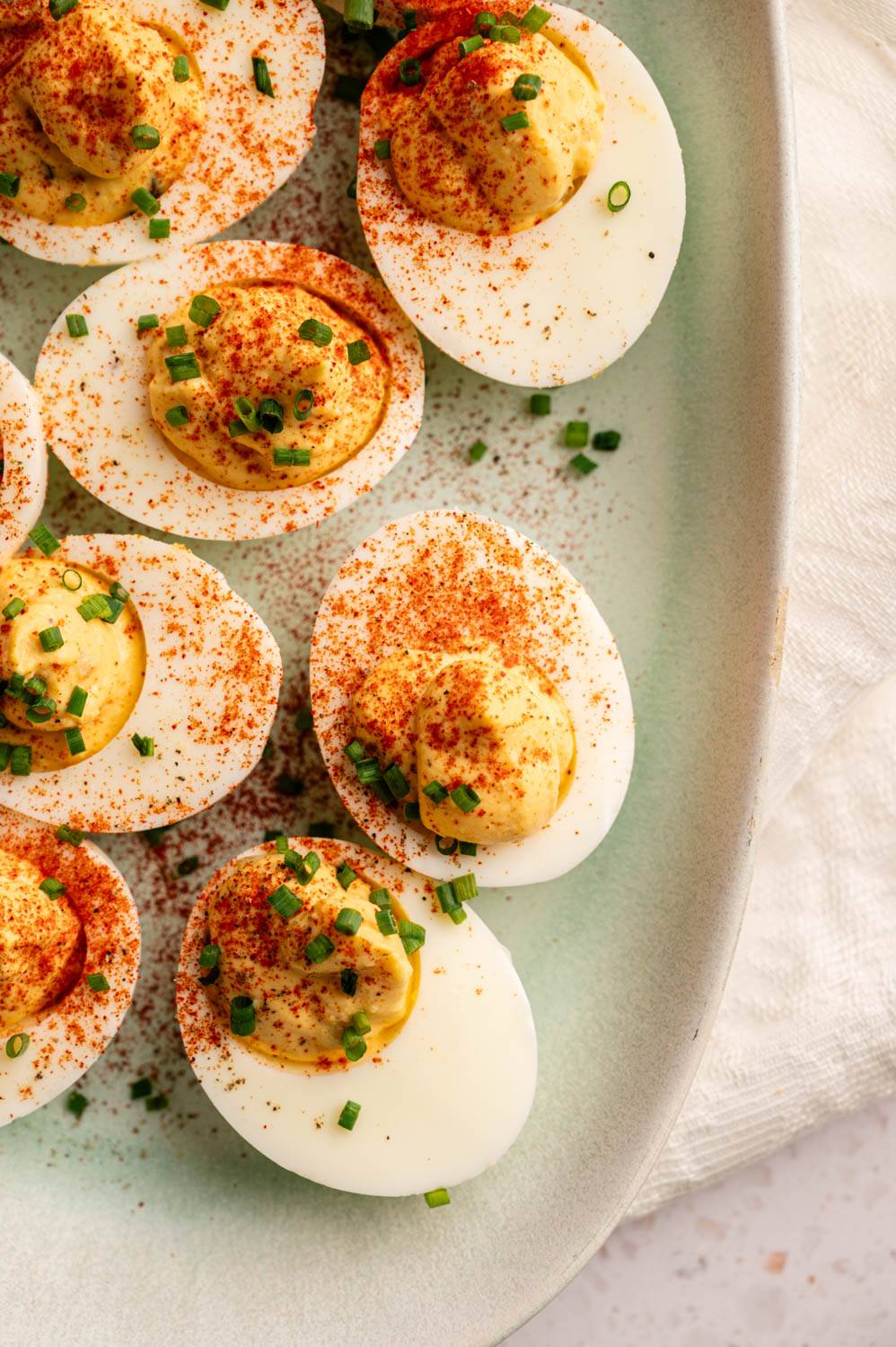 Close-up of deviled eggs on a light green plate, garnished with paprika and chopped chives. The eggs have a creamy yellow filling.