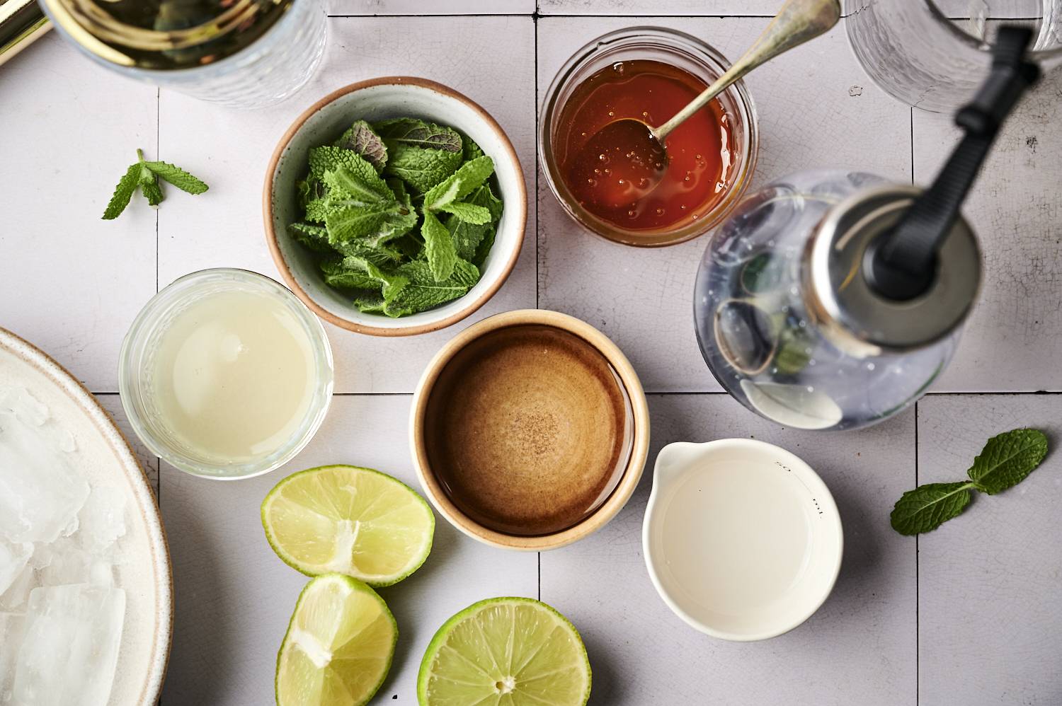 An overhead view of ingredients for a drink, including fresh mint, lime halves, honey, and liquid measurements on a rustic surface.