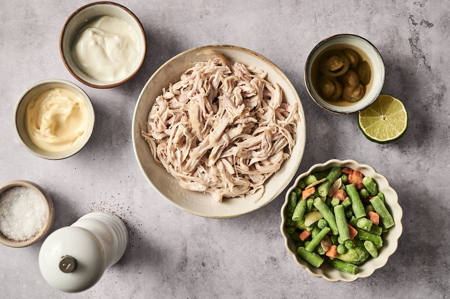 Shredded chicken, frozen mixed vegetables, mayonnaise, sour cream, pickled jalapeños, and seasonings on a table.
