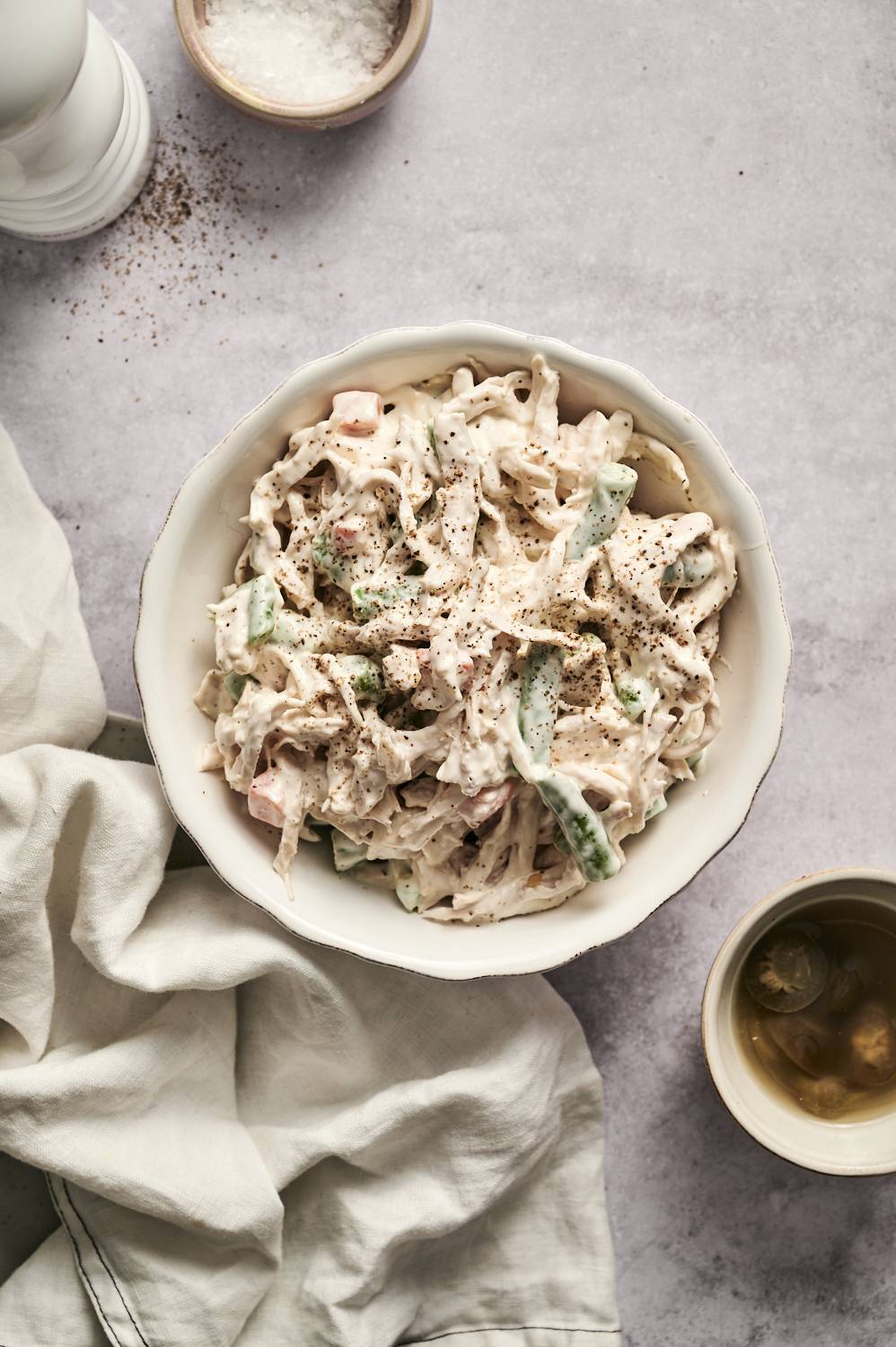A bowl of creamy chicken salad mixed with shredded chicken, vegetables, and dressing, garnished with black pepper.