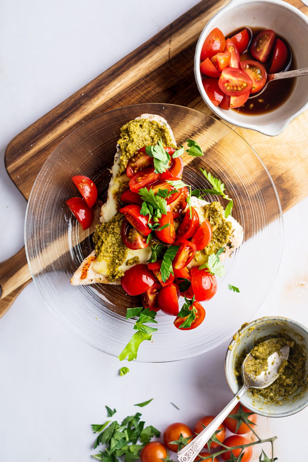 Grilled Margherita Chicken breast with basil pesto, cherry tomatoes, mozzarella cheese, and herbs on a glass plate.