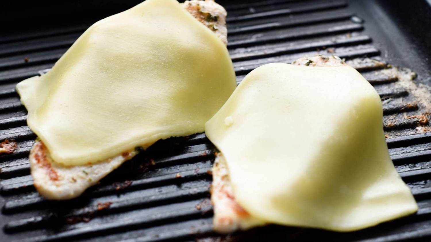 Herb chicken breast on the grill with slices of mozzarelle cheese.