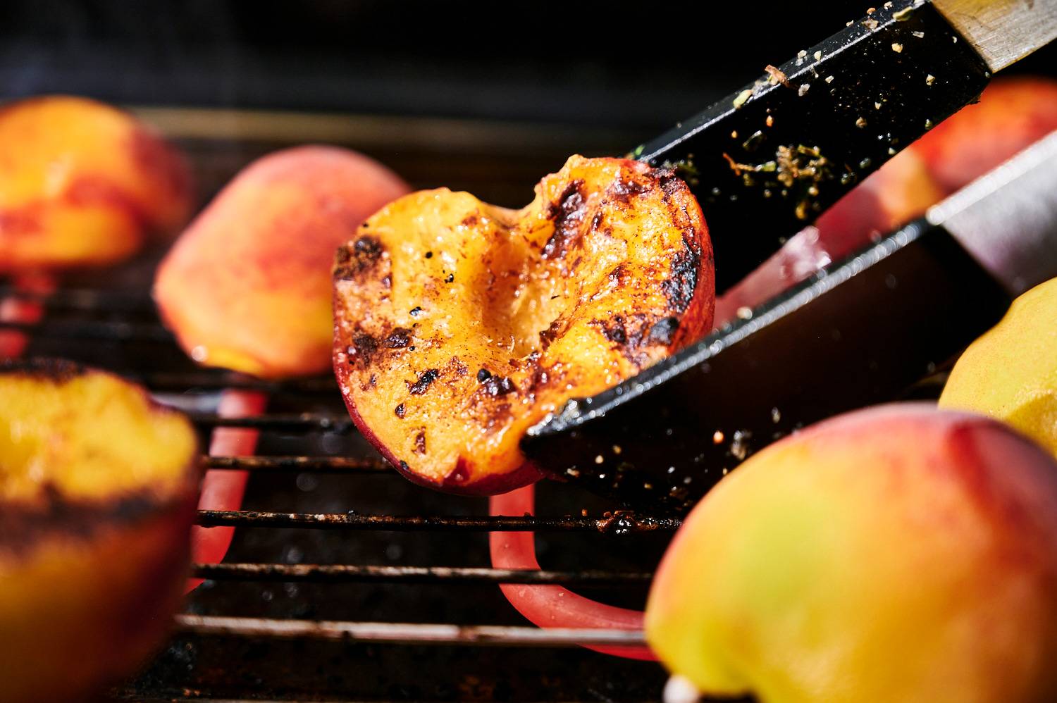 Fresh grilled peaches being picked up by tongs off a grill.