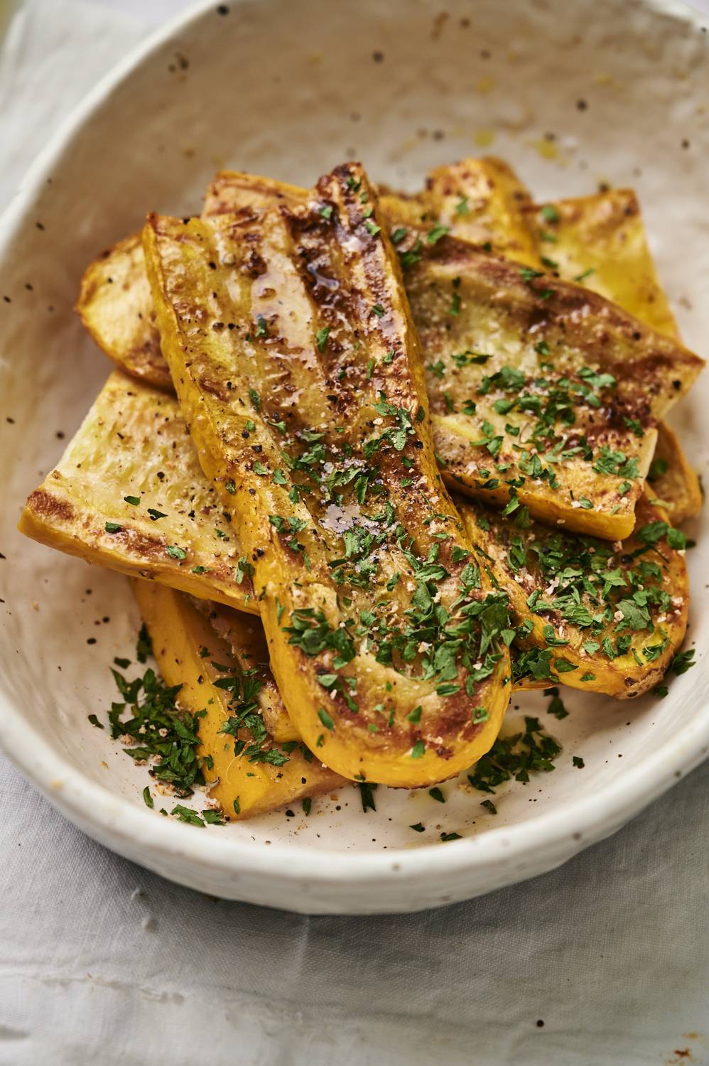 Grilled yellow squash slices topped with fresh herbs and seasoning, served in a white oval dish.