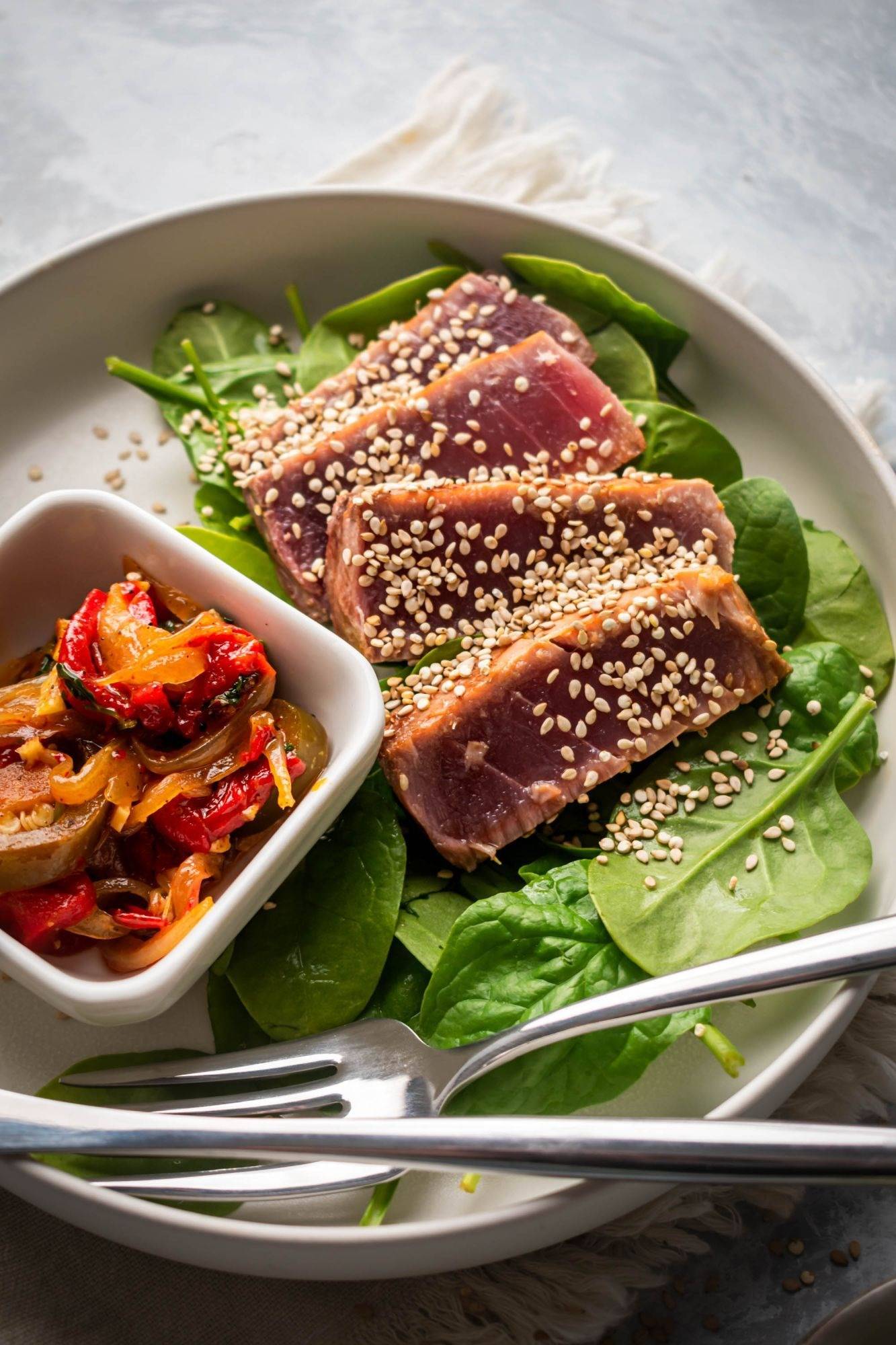 Sliced grilled ahi tuna with sesame seeds, green onions, and soy sauce on a plate with salad greens.