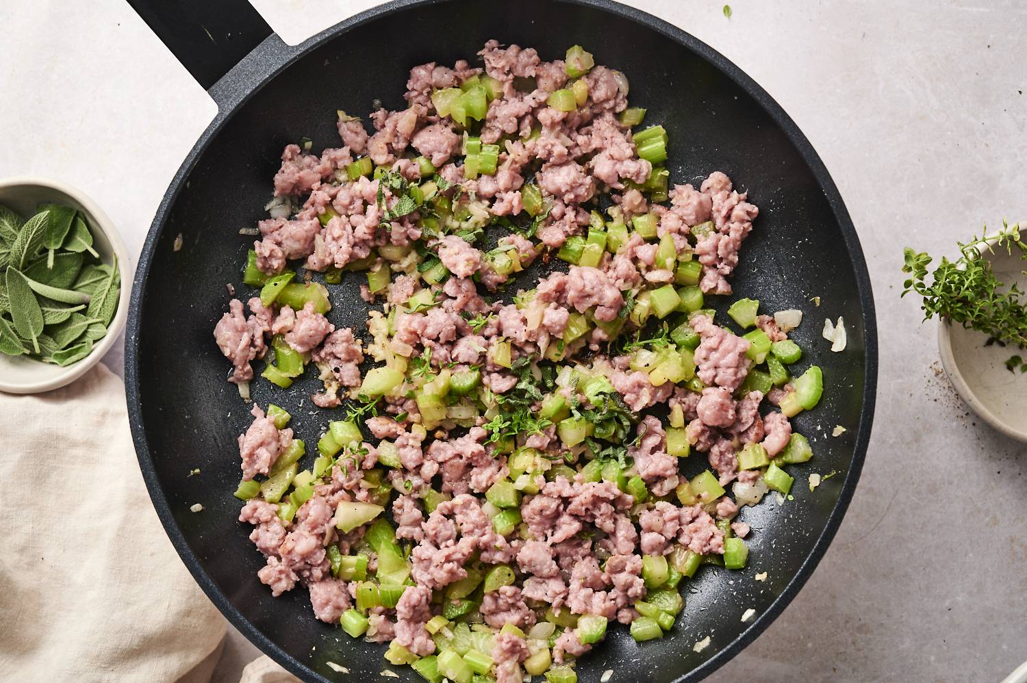 Sausage, celery, fresh hebrs, and onion being sauteed in a cast iron pan.