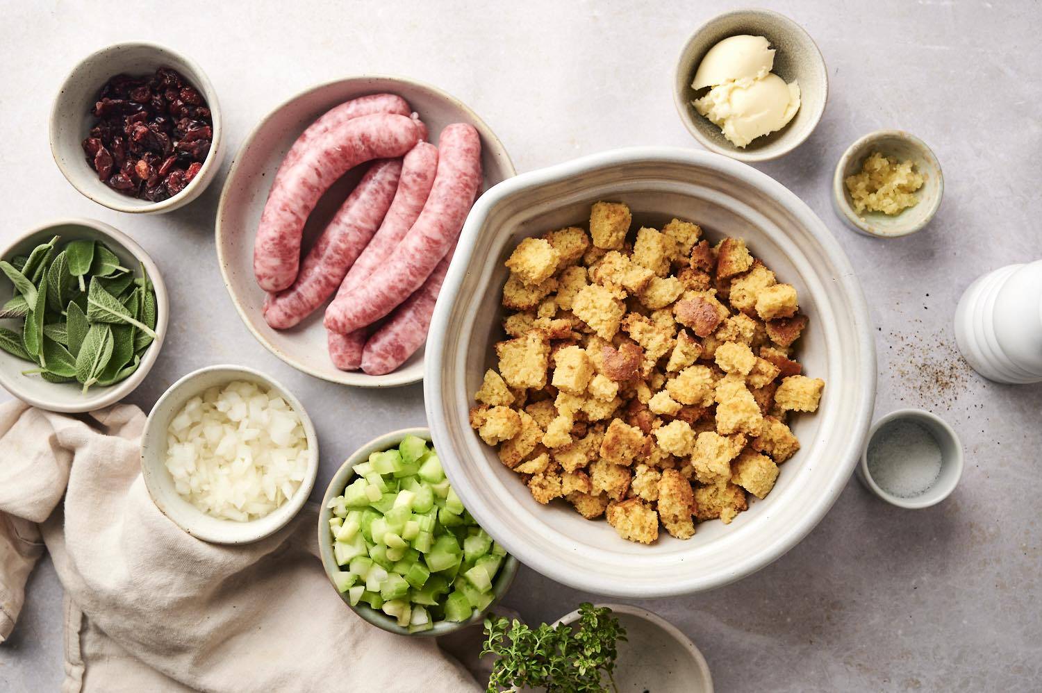 Ingredients for sausage stuffing laid out, including onions, celery, cornbread croutons, sausage and spices.