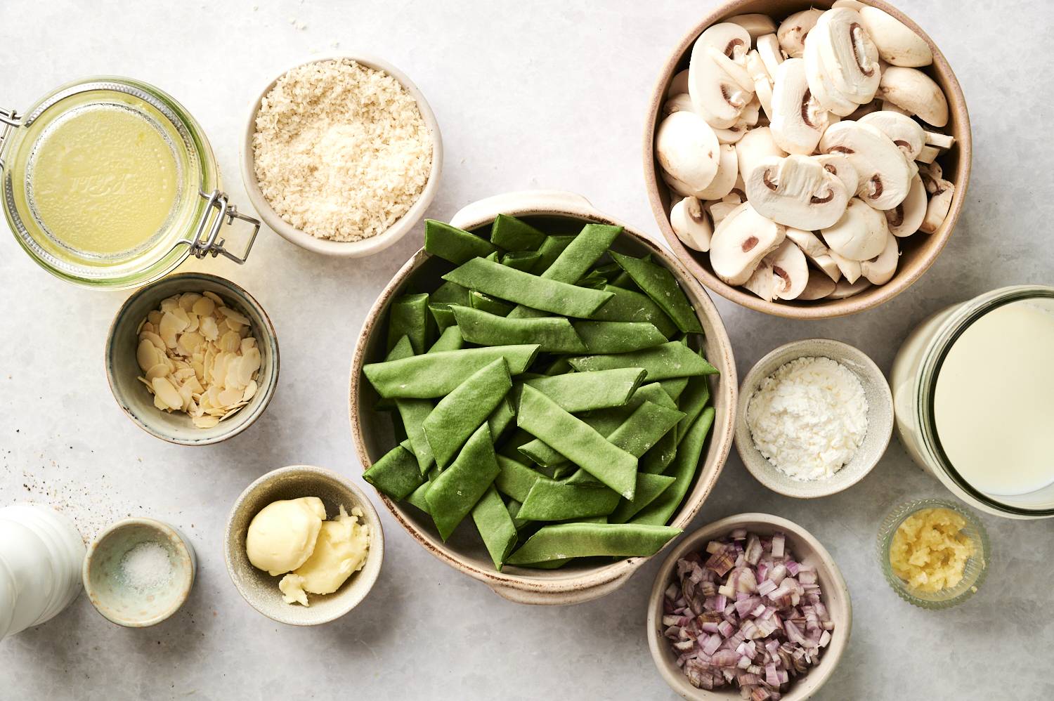 The ingredients to make healthy green bean casserole laying in bowls on the counter.