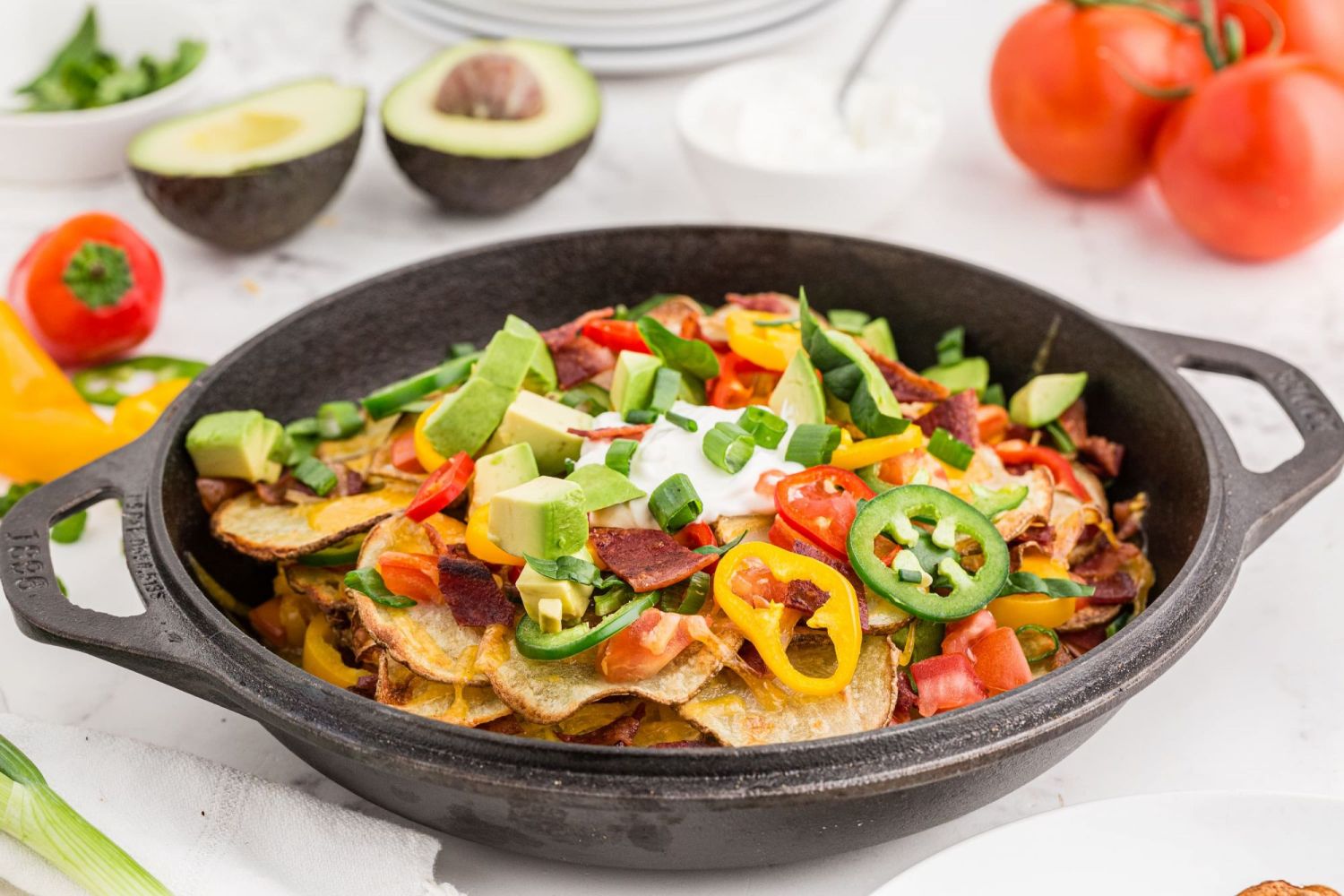 Baked Irish Nachos with melted cheddar cheese, crispy potatoes, bacon, bell peppers, and avocado in a skillet.