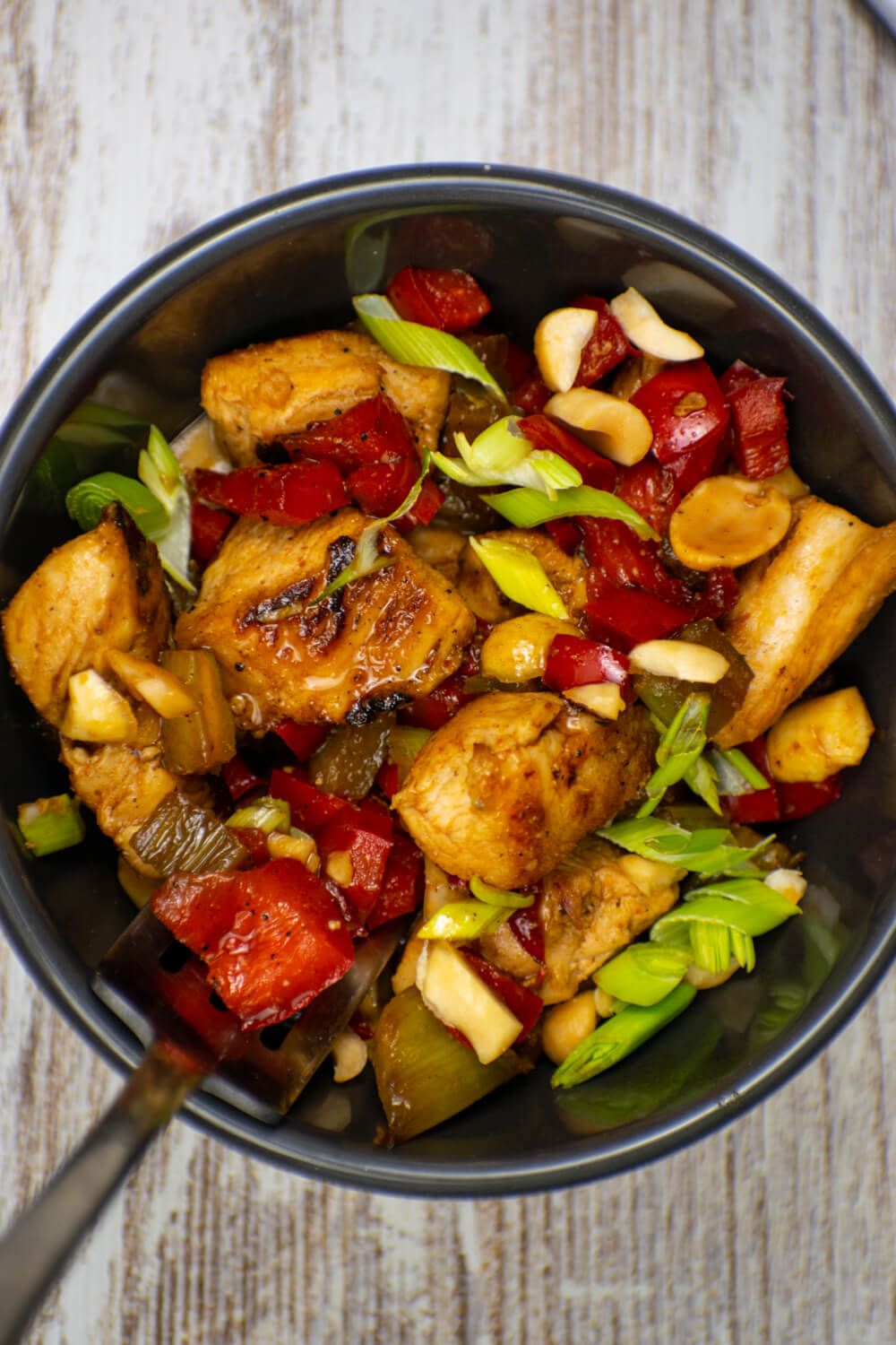 Kung Pao Chicken with chicken breast, red peppers, and green onions in a bowl.