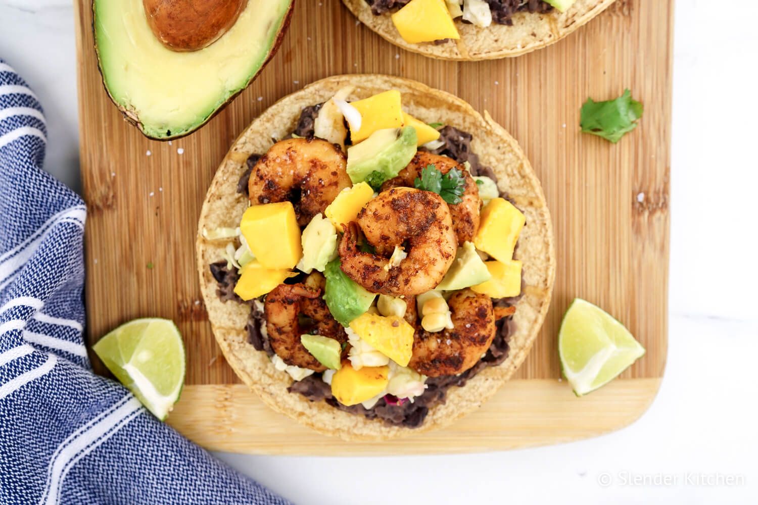 Mango Shrimp Tostadas with avocado, corn, black beans, cabbage, and mango on a cutting board.