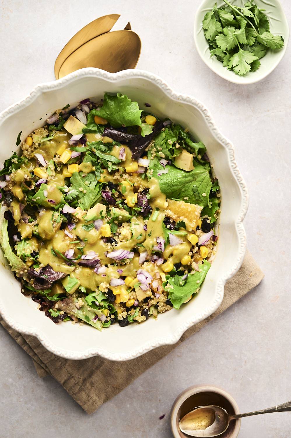 A bowl of Mexican quinoa salad with greens, black beans, corn, avocado, and creamy dressing, garnished with fresh cilantro.