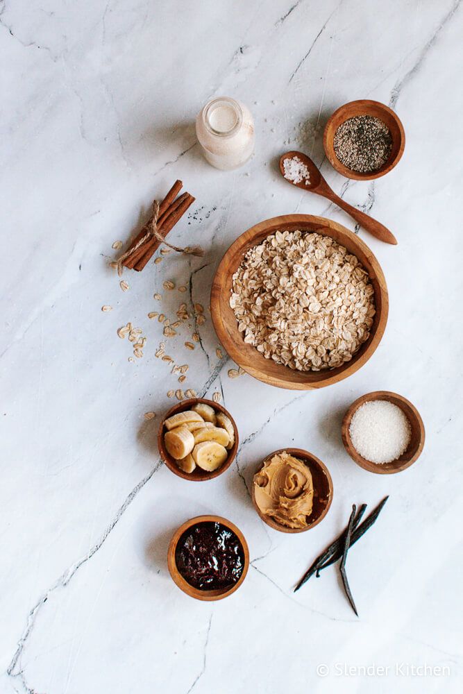 Peanut butter and jelly overnight oats ingredients in small containers including oats, jelly, peanut butter, cinnamon, milk, and more. 