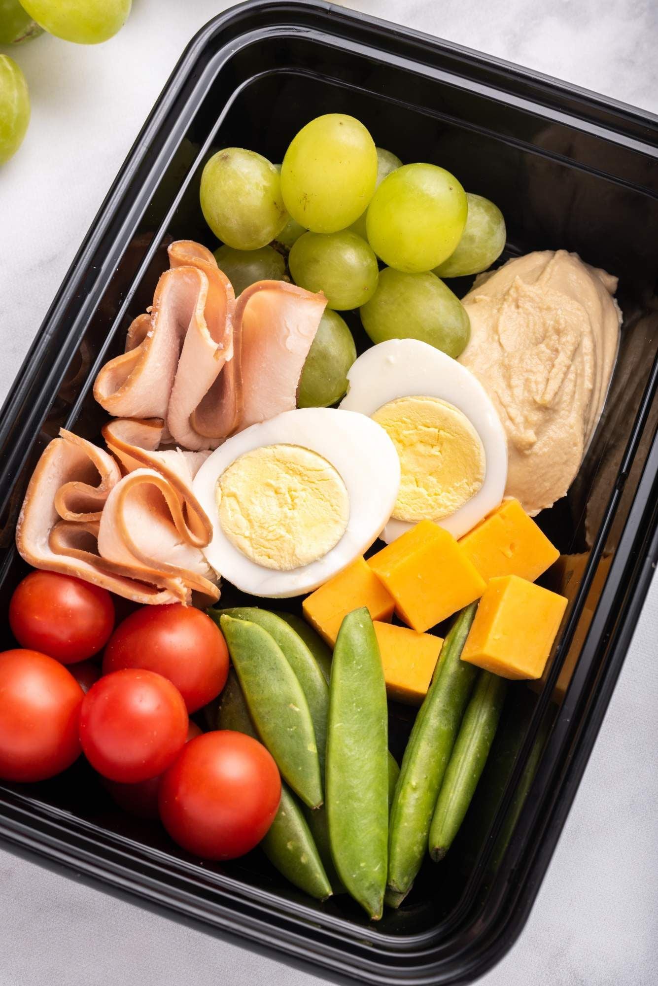 Copycat protein snack box with hard boiled eggs, snap peas, deli turkey, cheddar cheese, and grapes.